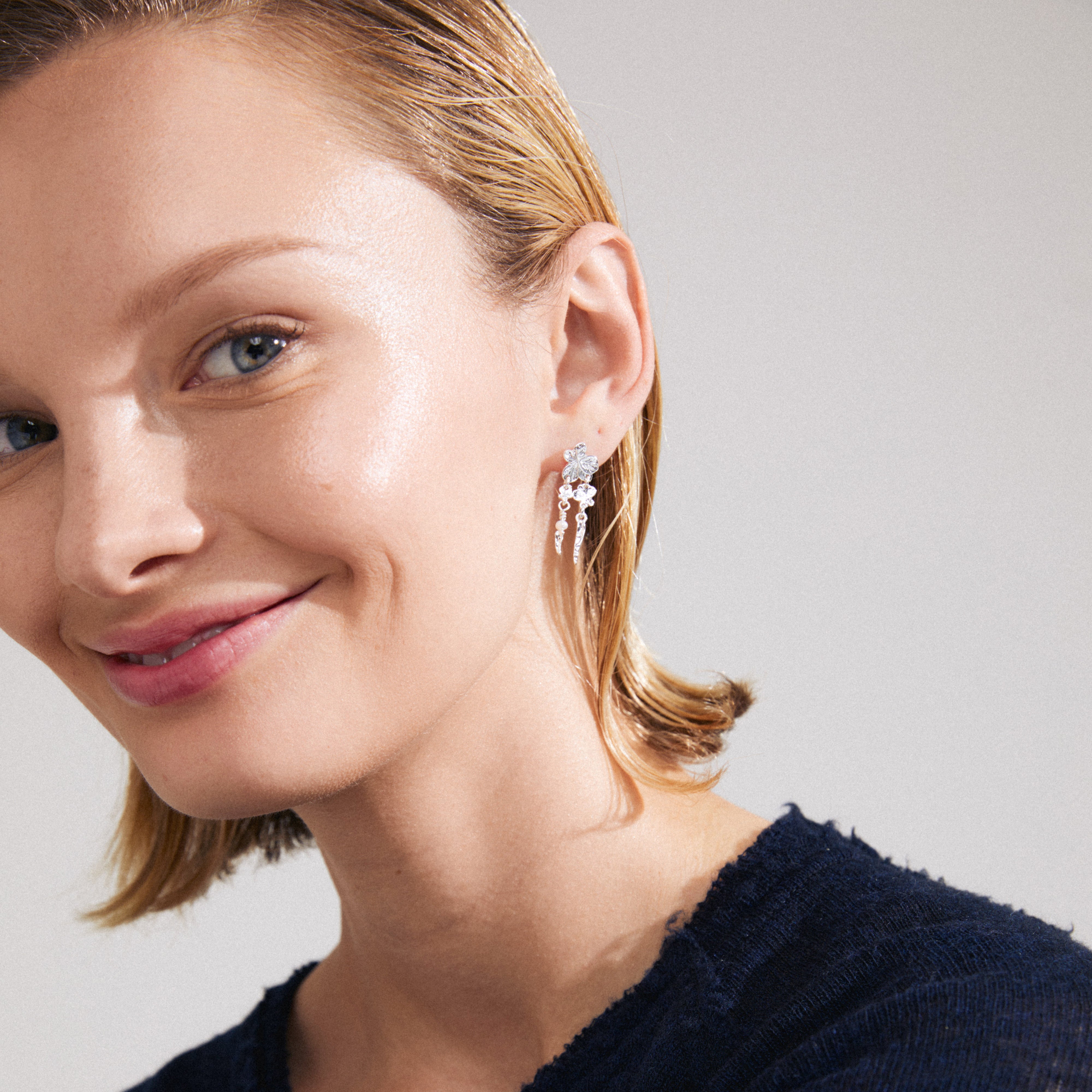 ZHURI silver-plated earrings featuring delicate floral motifs and a petite freshwater pearl, worn by a smiling woman, highlighting their romantic and playful style.