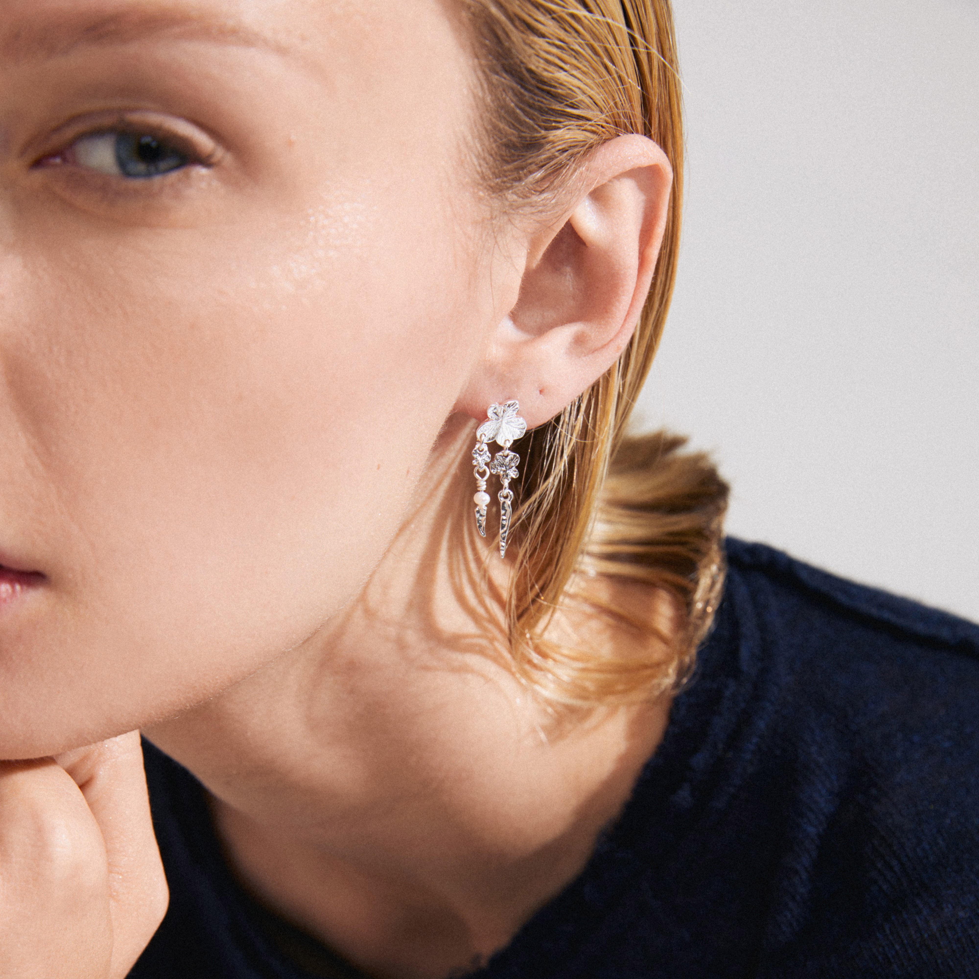 ZHURI earrings silver-plated with delicate floral motifs and a freshwater pearl, worn by a woman, adding elegance and playfulness to her style.