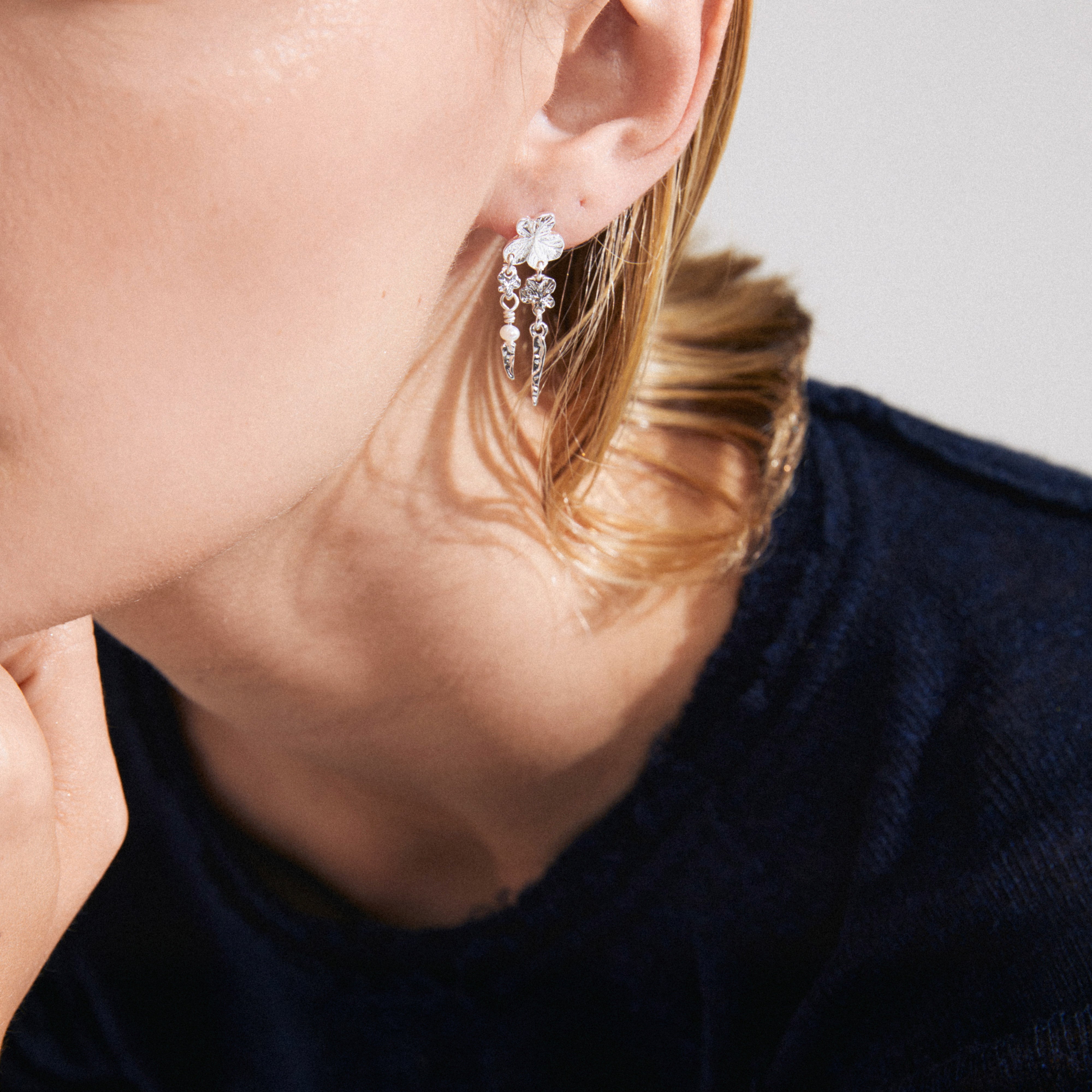 ZHURI earrings silver-plated, featuring a floral motif, pearl, and delicate charms, showcased on an ear. Elegant and playful, perfect for any occasion.