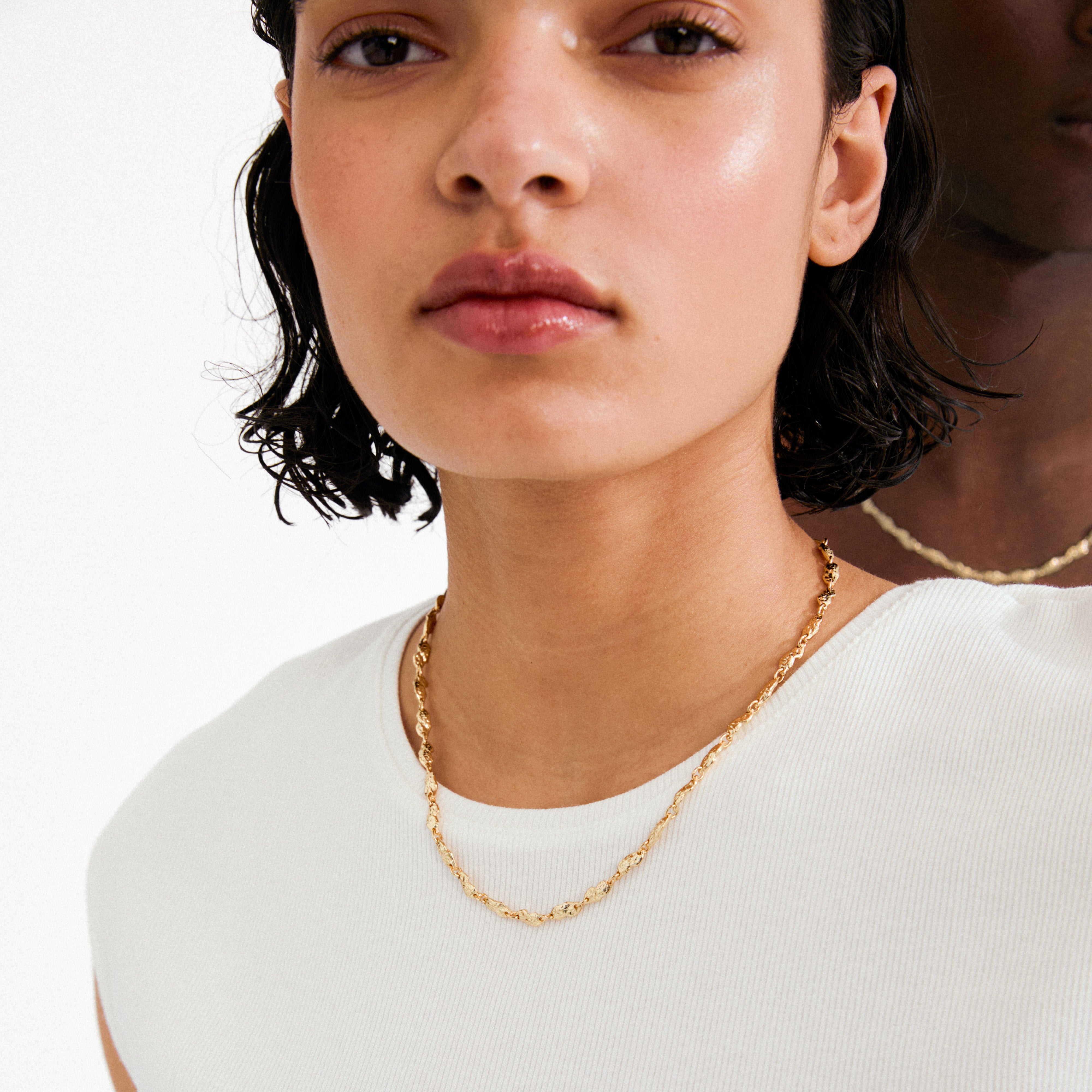 Close-up of a person wearing Pilgrim's gold-plated ELIYAH necklace, showcasing delicate nature-inspired links and a textured finish against a white ribbed sleeveless top.