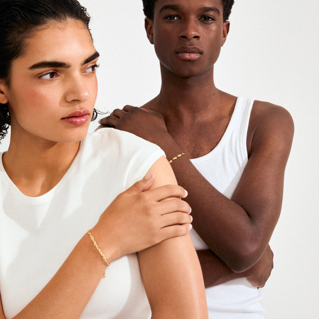 Two individuals display Pilgrim's ELIYAH gold-plated bracelet, showcasing its textured, nature-inspired links on their wrists against a minimalist setting.