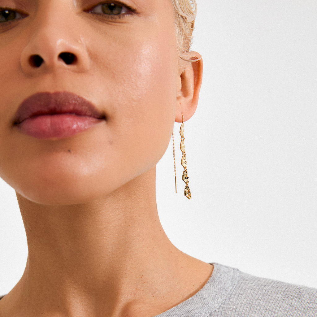 Close-up of a person's ear wearing ELIYAH gold-plated chain earrings by Pilgrim, showcasing textured curb links and sculptural design for stylish, sustainable flair.