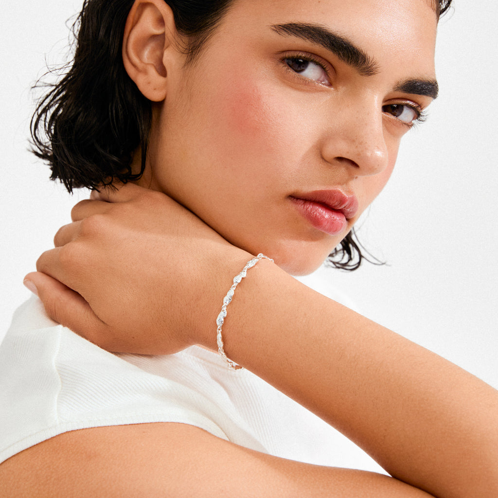 Young woman wearing Pilgrim’s ELIYAH bracelet, showcasing its silver-plated, rustic texture and minimalist design on her wrist, complementing a simple outfit.