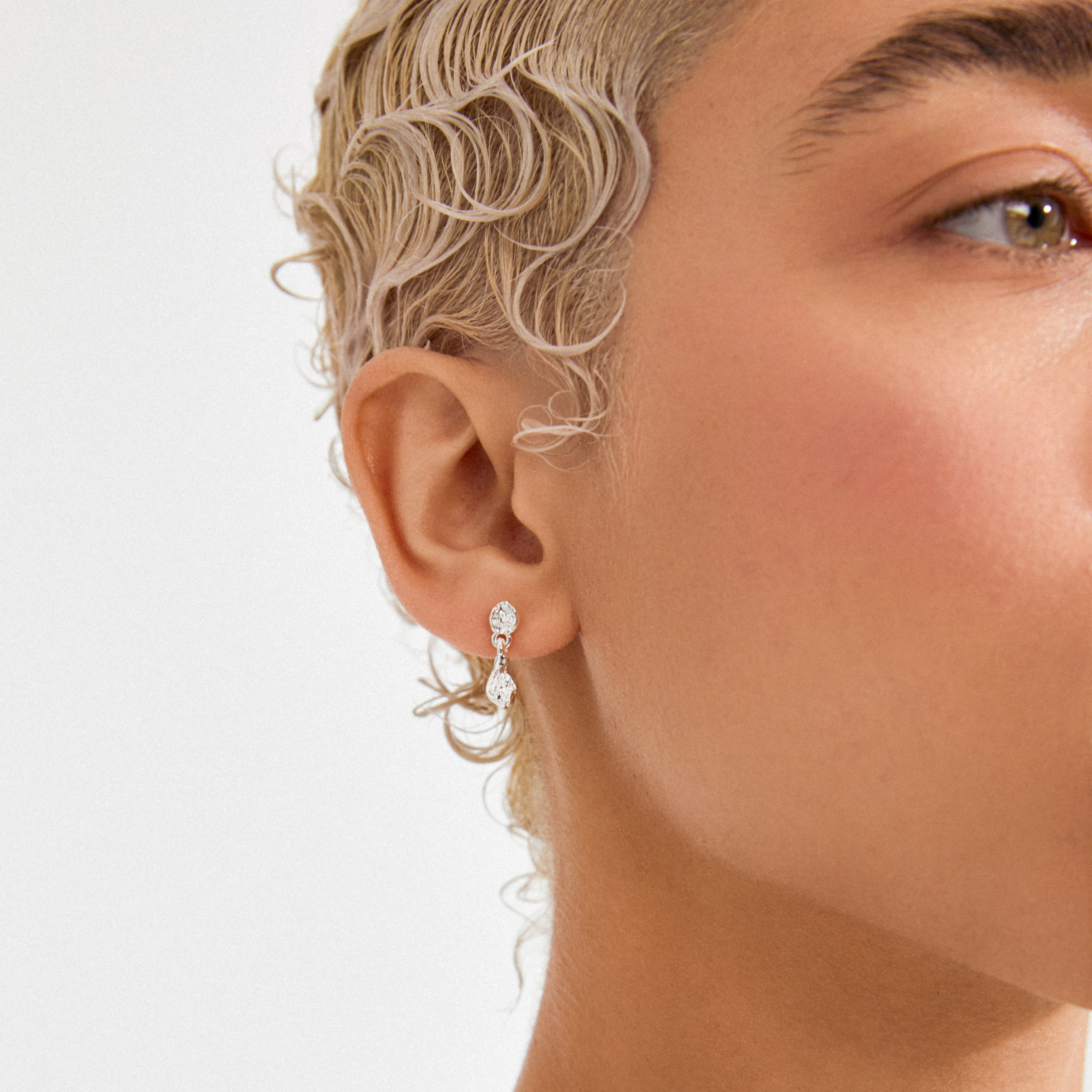 Side profile highlighting ELIYAH silver-plated drop earrings with diamond-like stones, styled with wet-look platinum-blonde waves, showcasing Pilgrim's timeless, trendy craftsmanship.