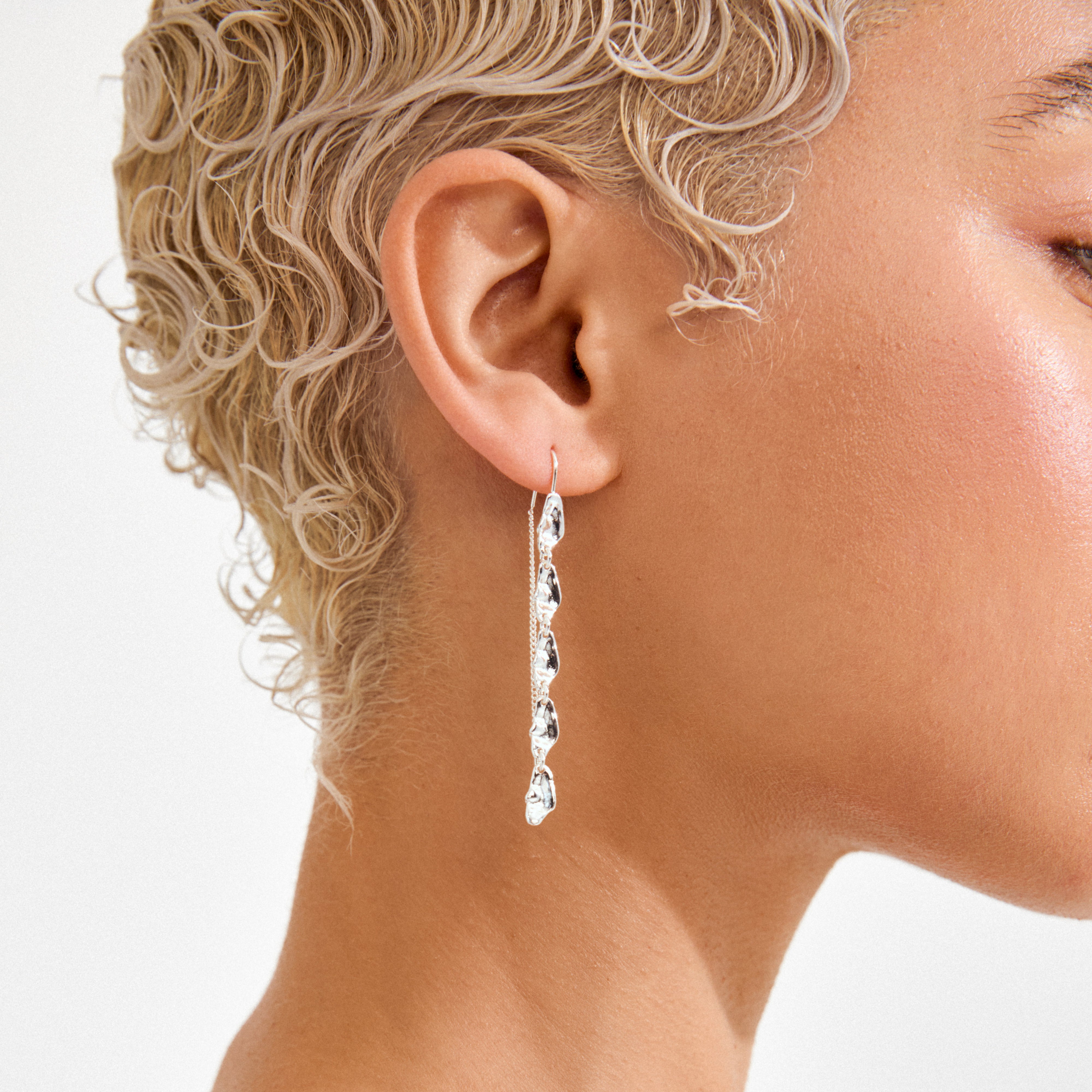 Close-up of a person's ear with ELIYAH chain earrings by Pilgrim, featuring silver-plated, dangling sculptural links that create a modern, flowing silhouette.