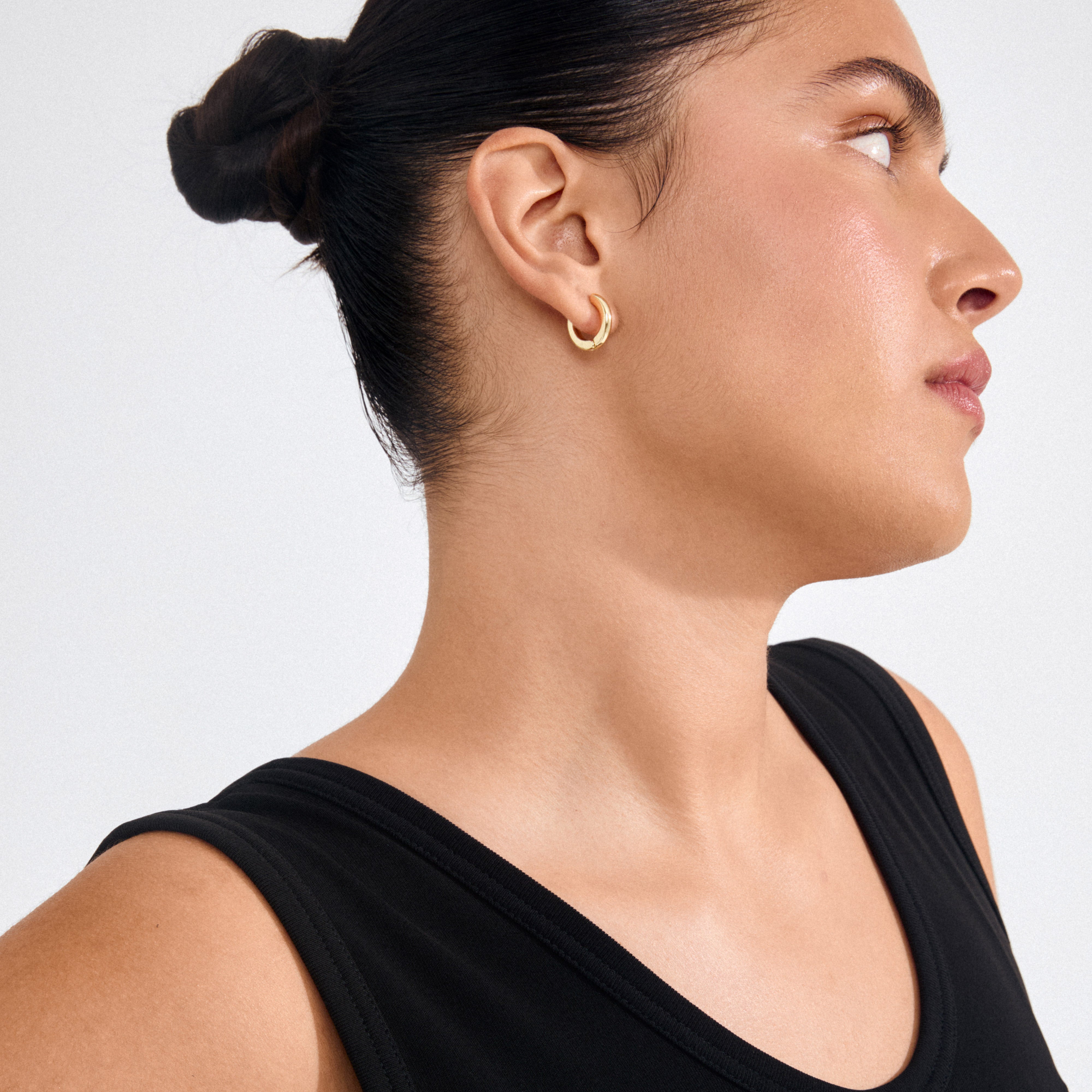 Person wearing TYRA chunky hoop earrings, gold-plated, showcasing their simple, classic, and chunky design. Perfect for a clean statement or layering for a personal touch.