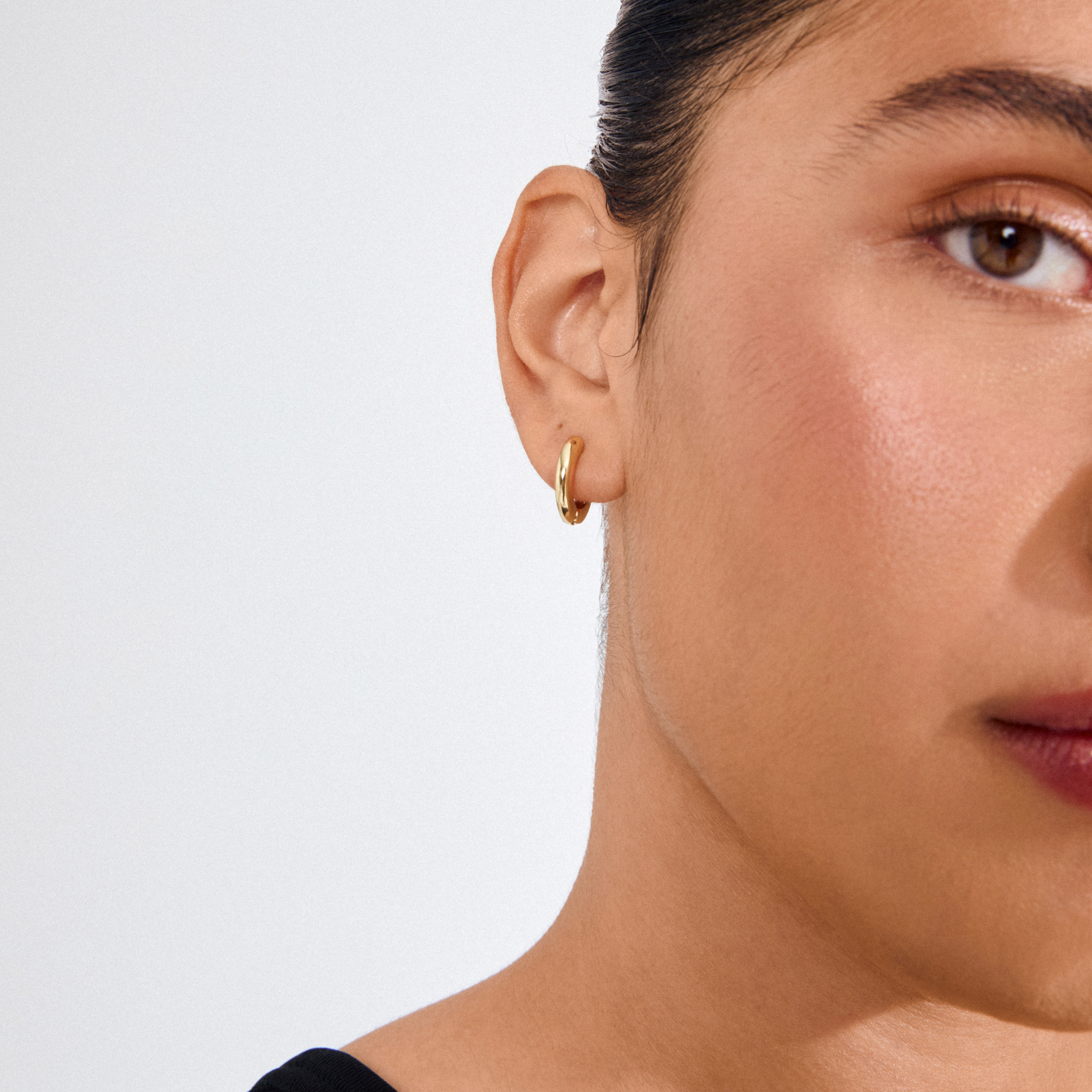 Close-up of a person's right ear wearing Pilgrim's TYRA chunky hoop earring, a gold-plated, classic design, highlighting simplicity and crafted from recycled materials for a stylish, sustainable look.