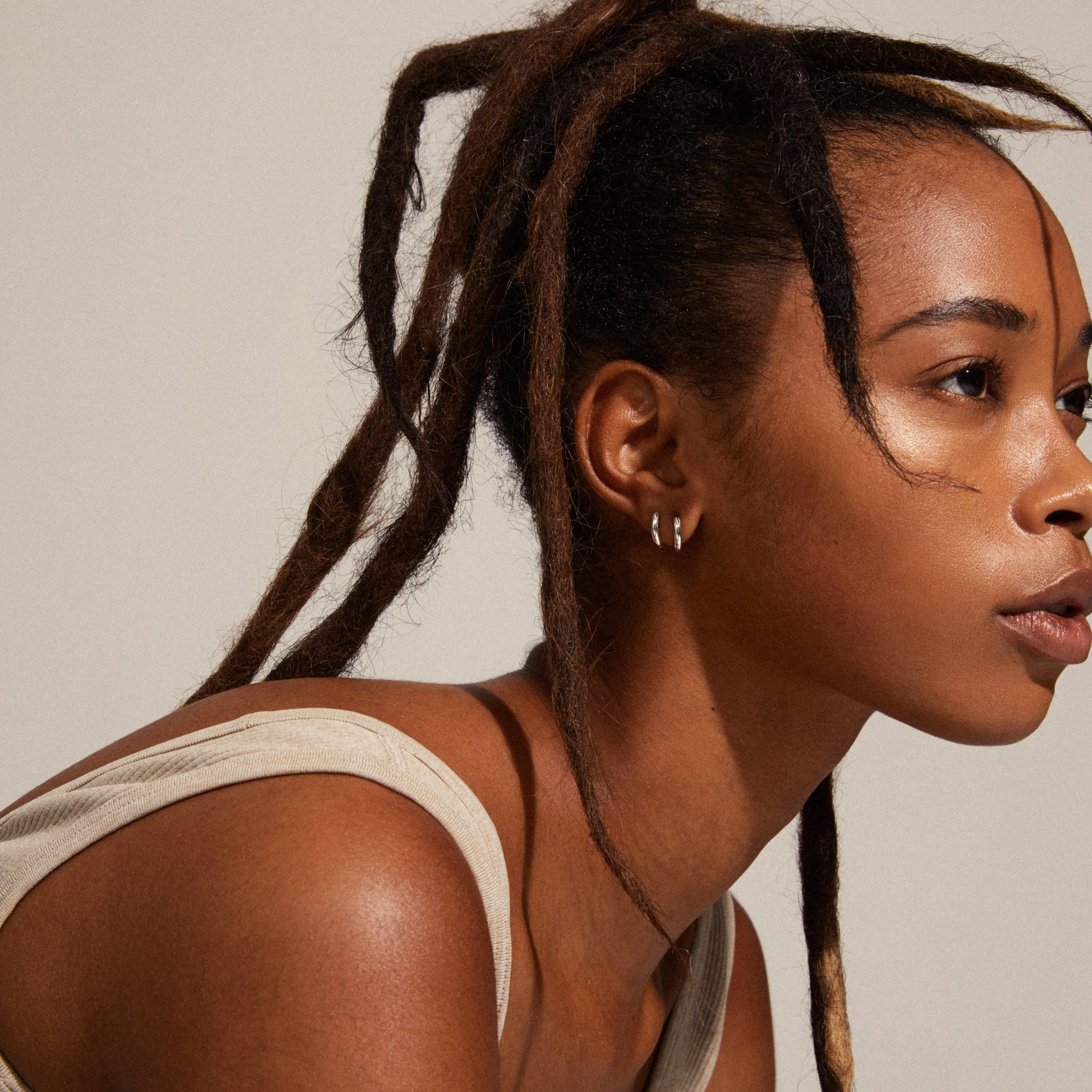 TYRA chunky mini hoop earrings in silver-plated finish, worn by a woman with dreadlocks, showcasing Pilgrim's stylish, eco-friendly design.