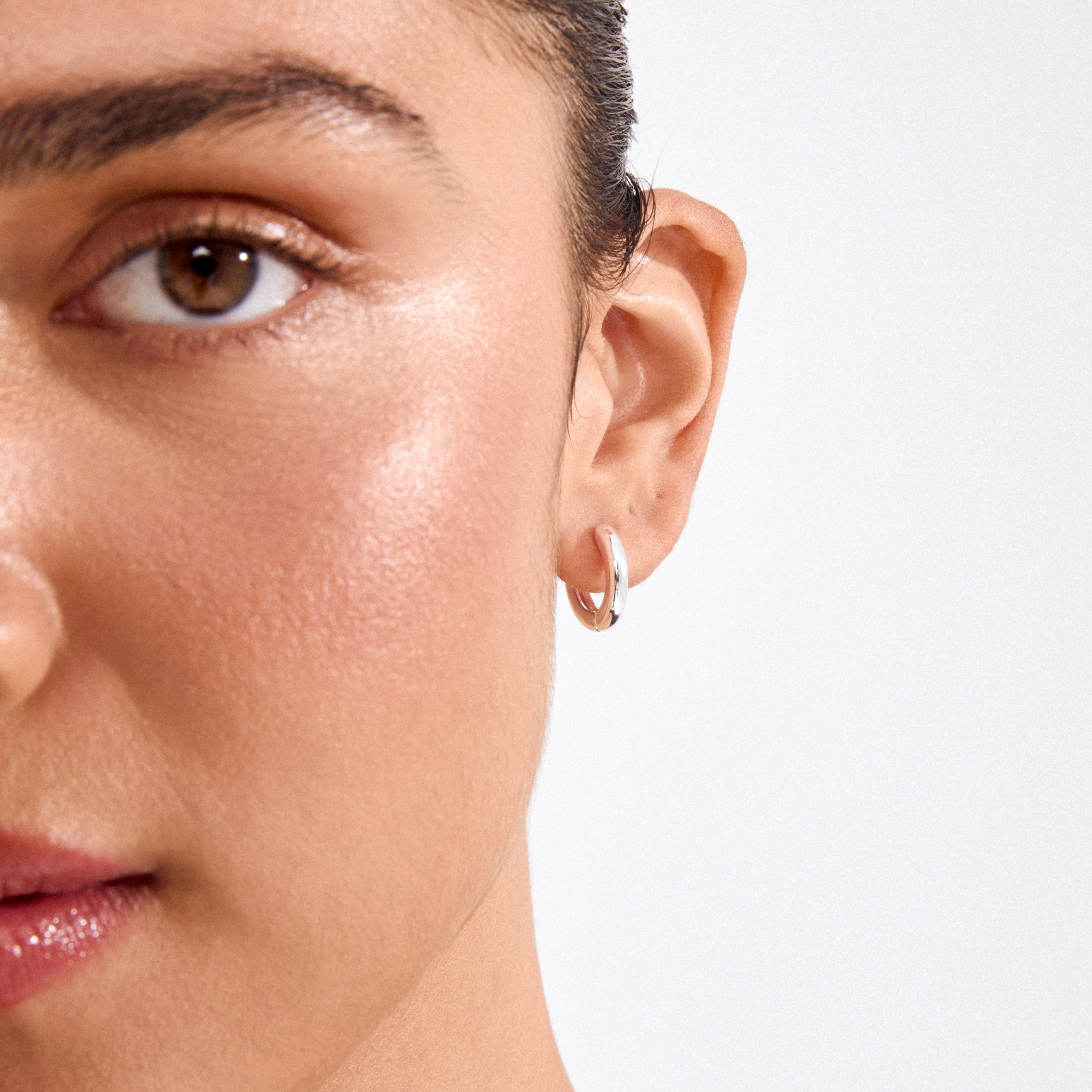 Close-up of a person's ear wearing TYRA chunky hoop earrings, silver-plated, showcasing their simple, classic design and chunky silhouette for a sleek, stylish look.