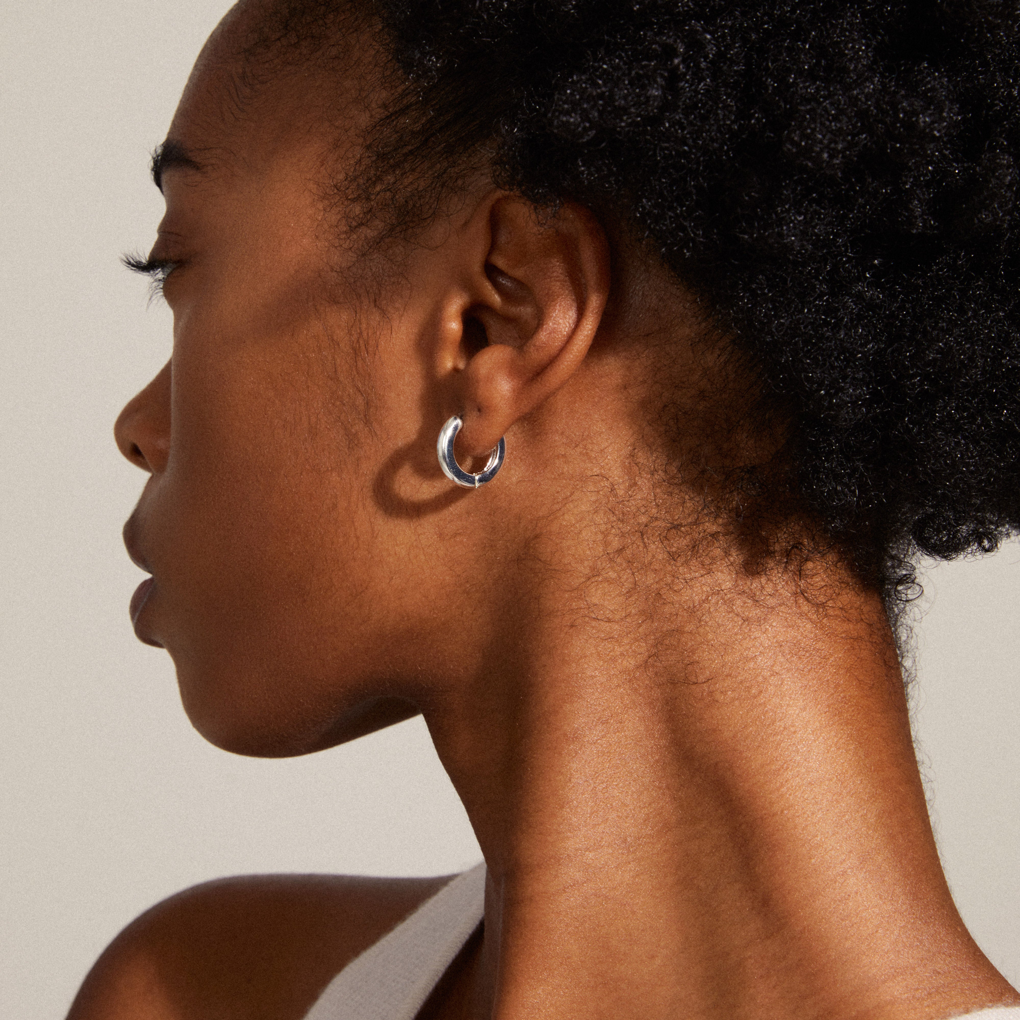 TYRA chunky hoop earrings, silver-plated, showcased on a woman's ear. These classic hoops from Pilgrim are stylish and eco-friendly, made from 99% recycled materials.