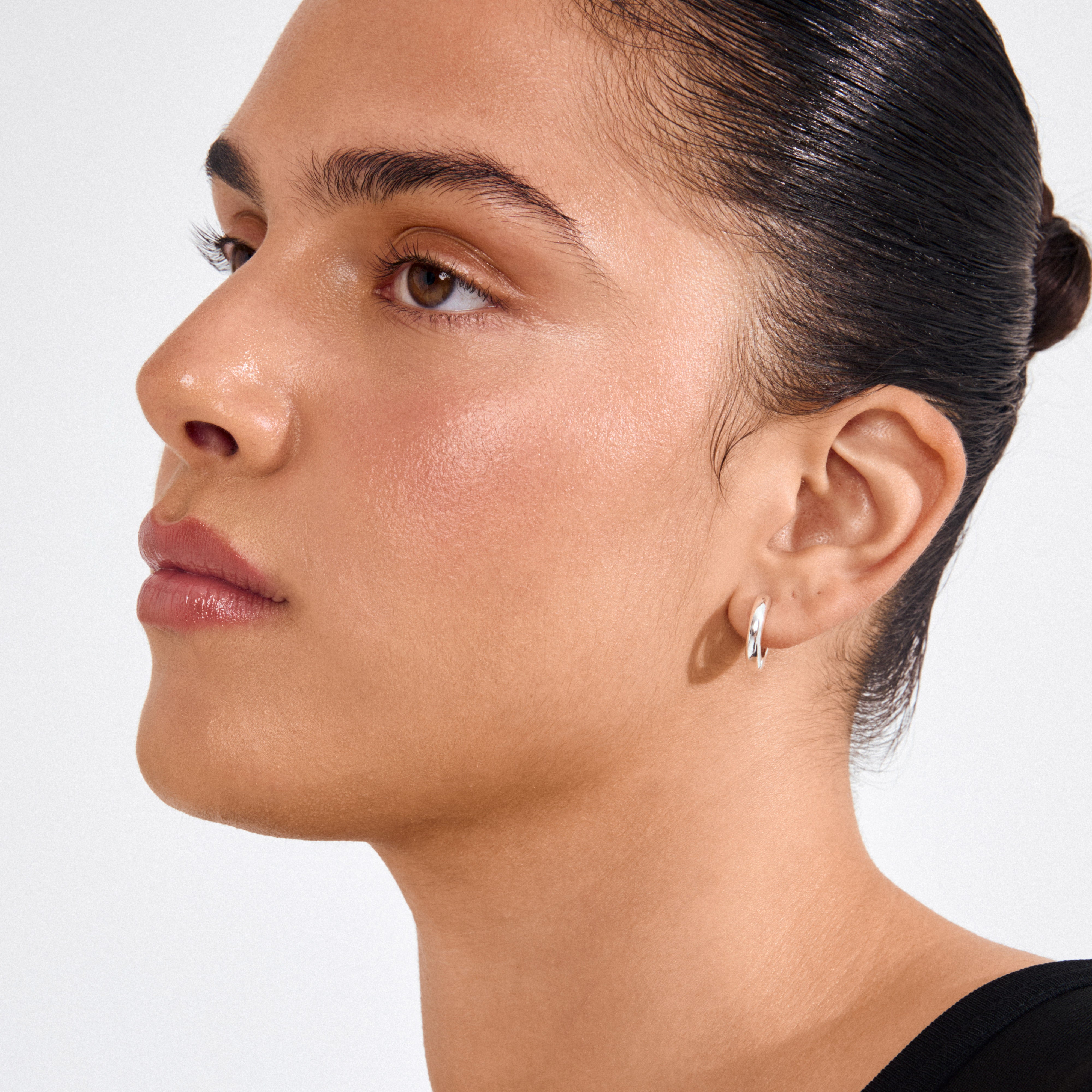Profile showcasing the TYRA chunky hoop earrings in silver-plated finish, highlighting their polished, sleek design on a young adult with a bun hairstyle.