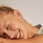 Woman wearing EDDY organic shaped mini huggie hoops gold-plated, eyes closed, smiling, showcasing the earrings' handcrafted and undulating design. Perfect for a curated ear look.