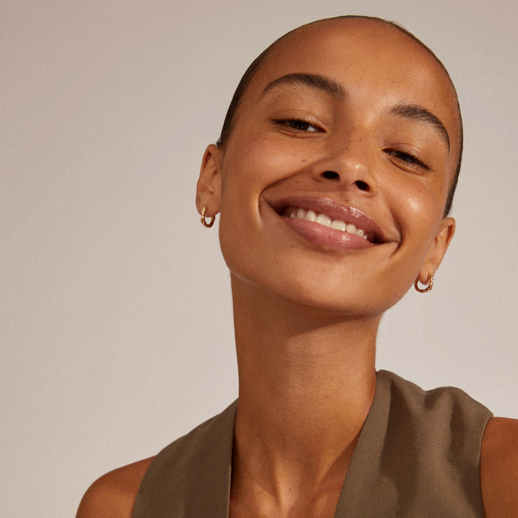 EDDY organic-shaped small hoops, gold-plated, worn by a smiling woman, showcasing their unique, wavy design and easy-to-use click lock.