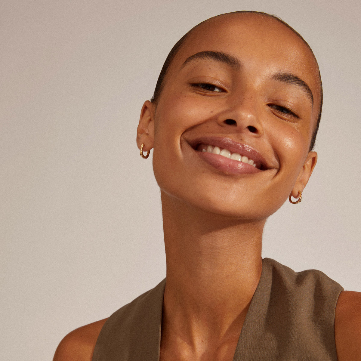 EDDY organic-shaped small hoops, gold-plated, worn by a smiling woman, showcasing their unique, wavy design and easy-to-use click lock.