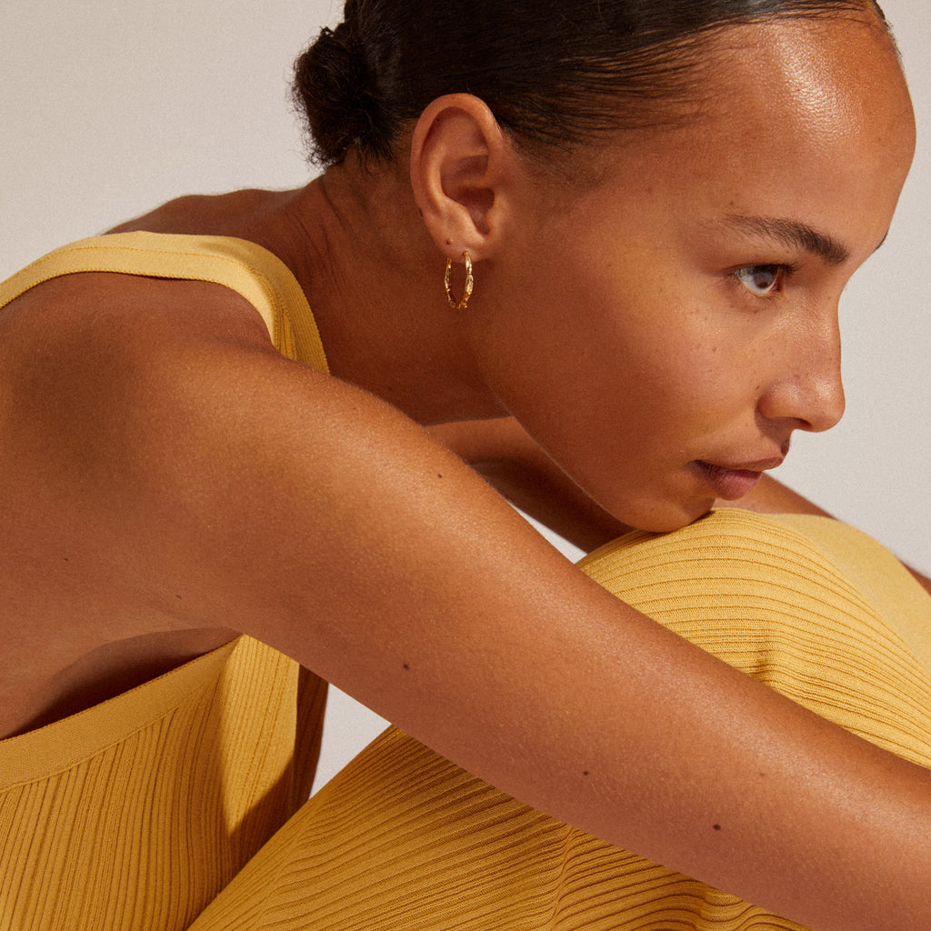 EDDY organic shaped large hoops gold-plated, displayed by a woman in a yellow dress, highlighting their handcrafted, unique design perfect for stylish adventures.