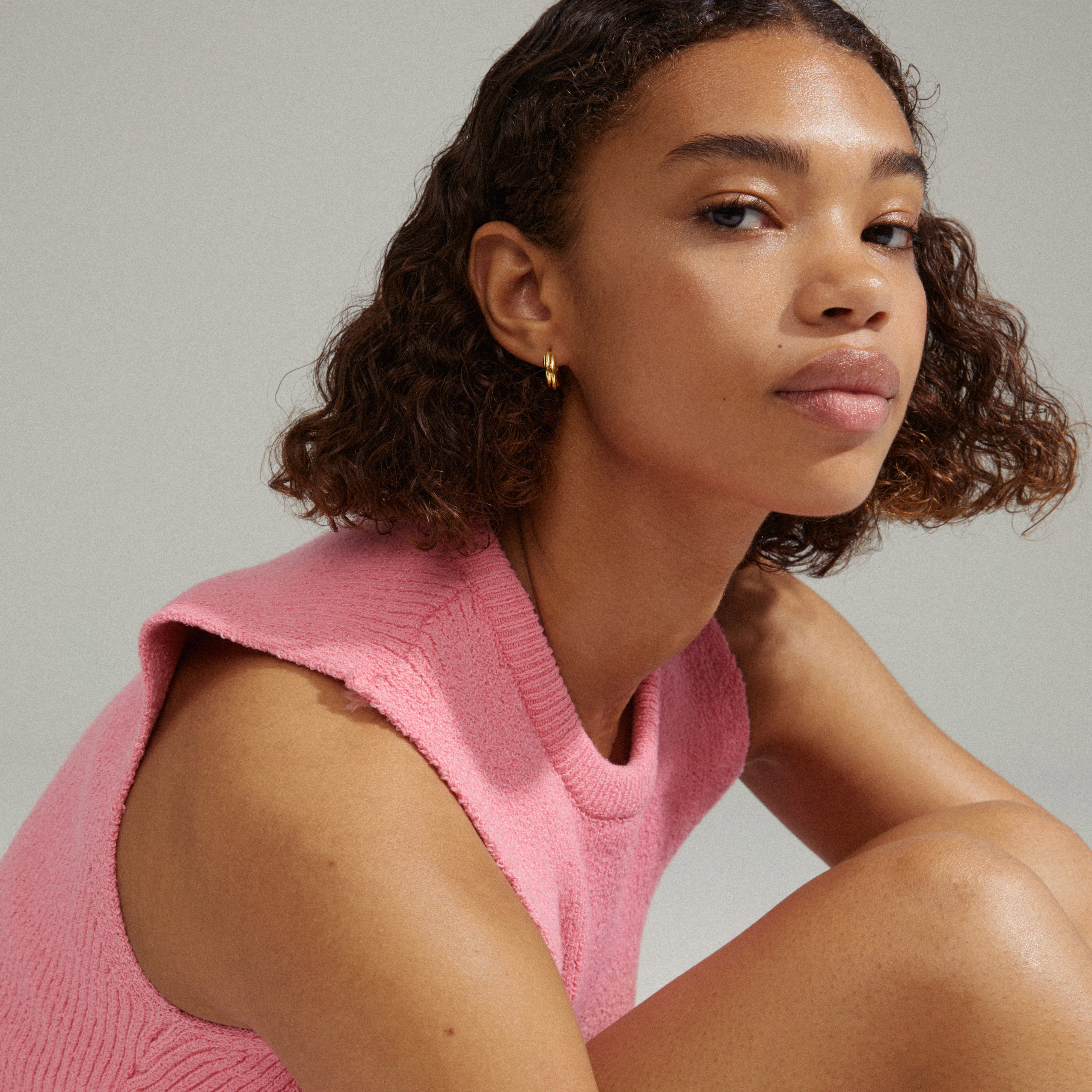 EDEA chunky huggie hoops gold-plated, worn by a woman in a pink shirt, showcasing the earrings' elegant, soft design suitable for both parties and everyday looks.