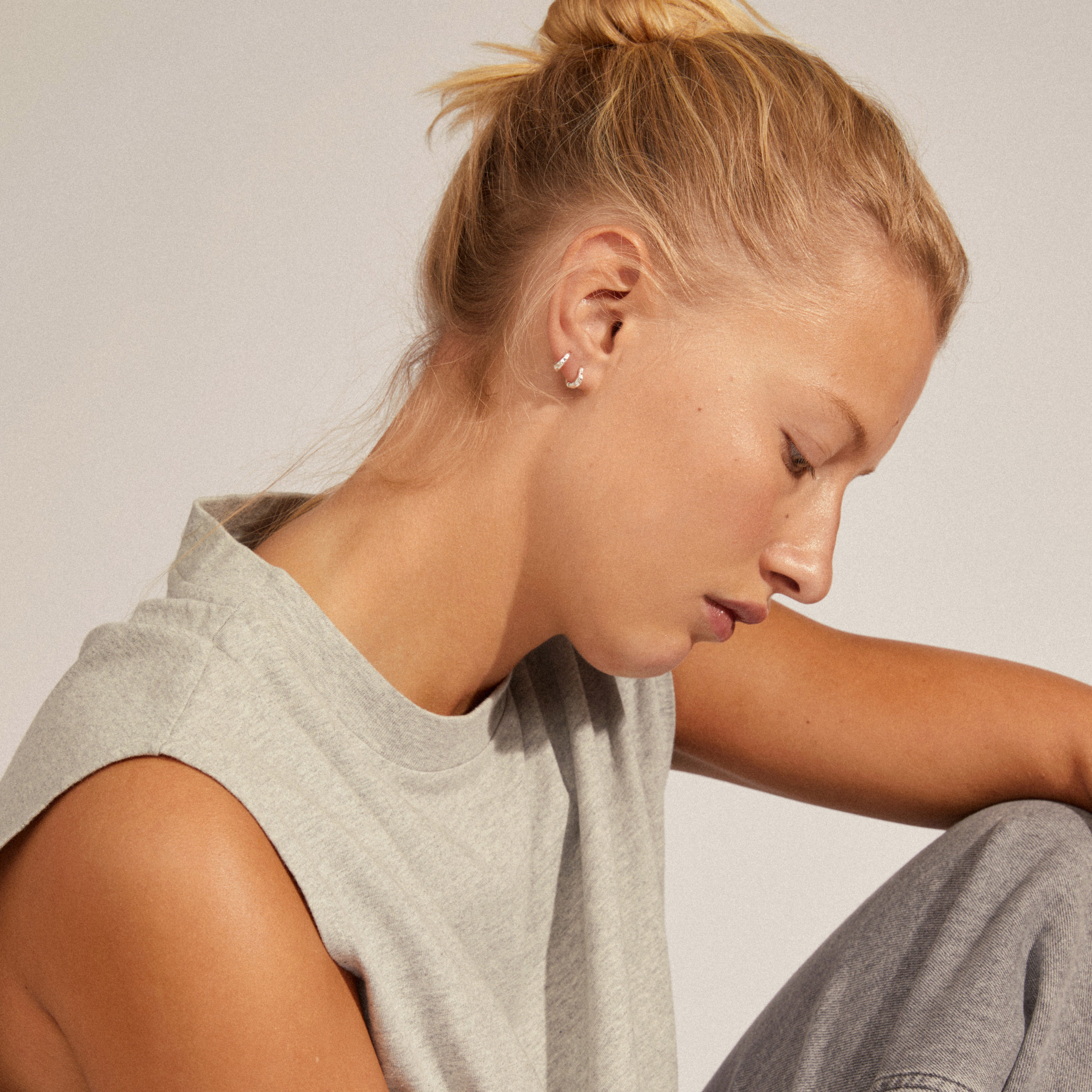 A woman wears EDDY organic shaped mini huggie hoops, silver-plated, showcasing their unique twisting form and elegant design.