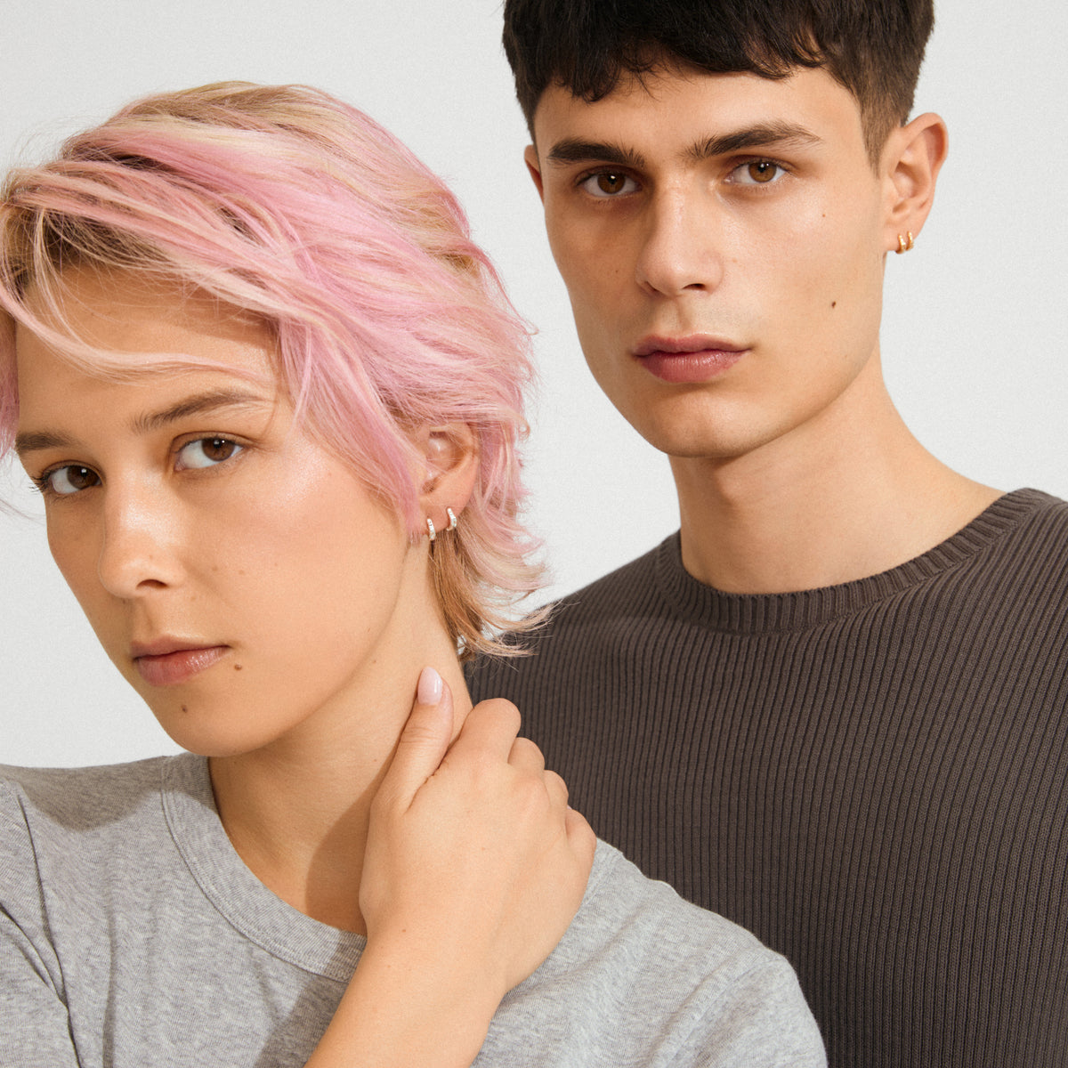 Two young adults wear Pilgrim's EDDY organic shaped mini huggie hoops, showcasing their silver-plated, twisting design in a close-up portrait.