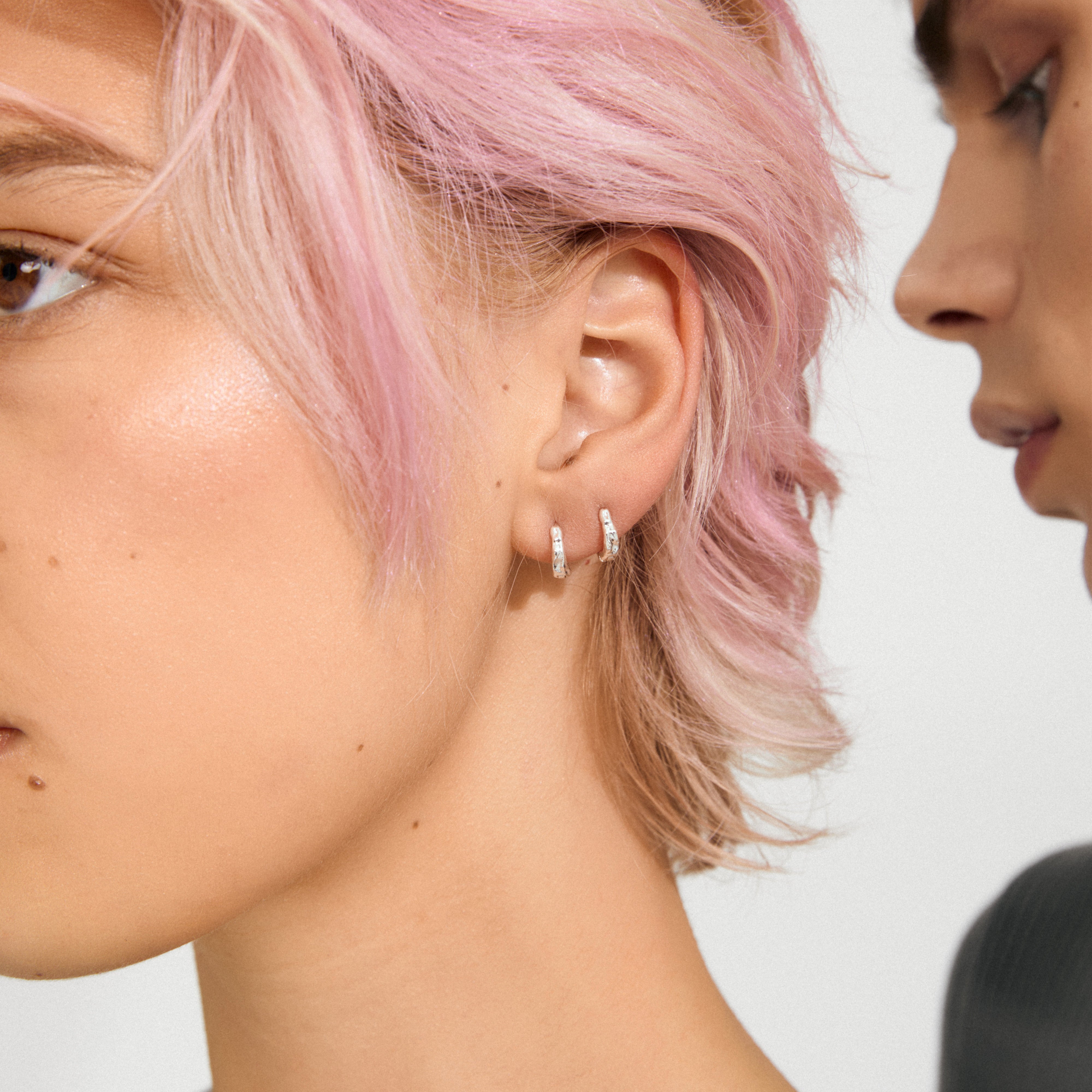 Profile view of pastel-pink haired person wearing EDDY organic shaped mini huggie hoops, silver-plated, highlighting their twisting, water-like form in a stylized shot.