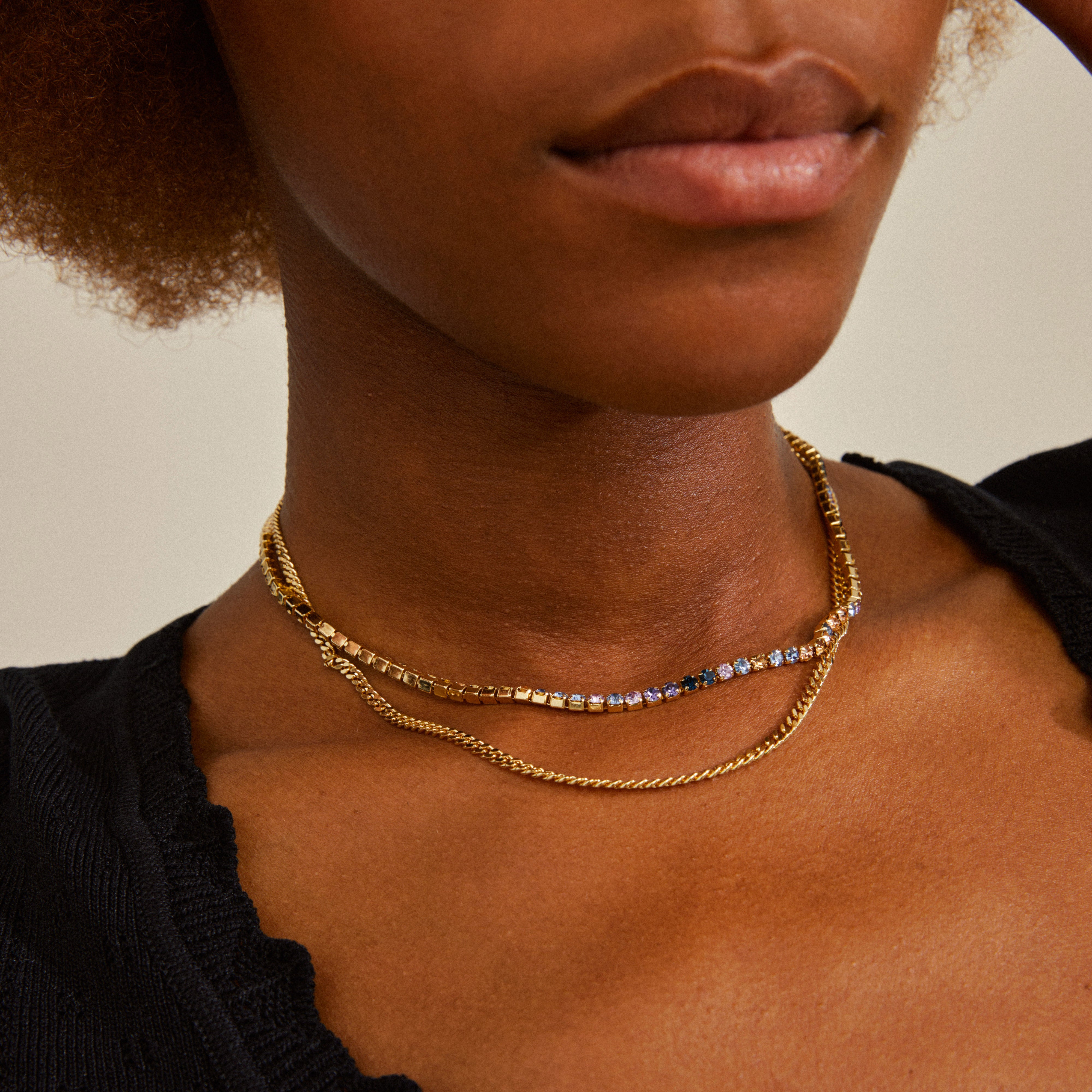 REIGN necklaces, 2-in-1 set, gold-plated, featuring a classic curb chain and sparkling blue and champagne crystals, elegantly worn by a woman.