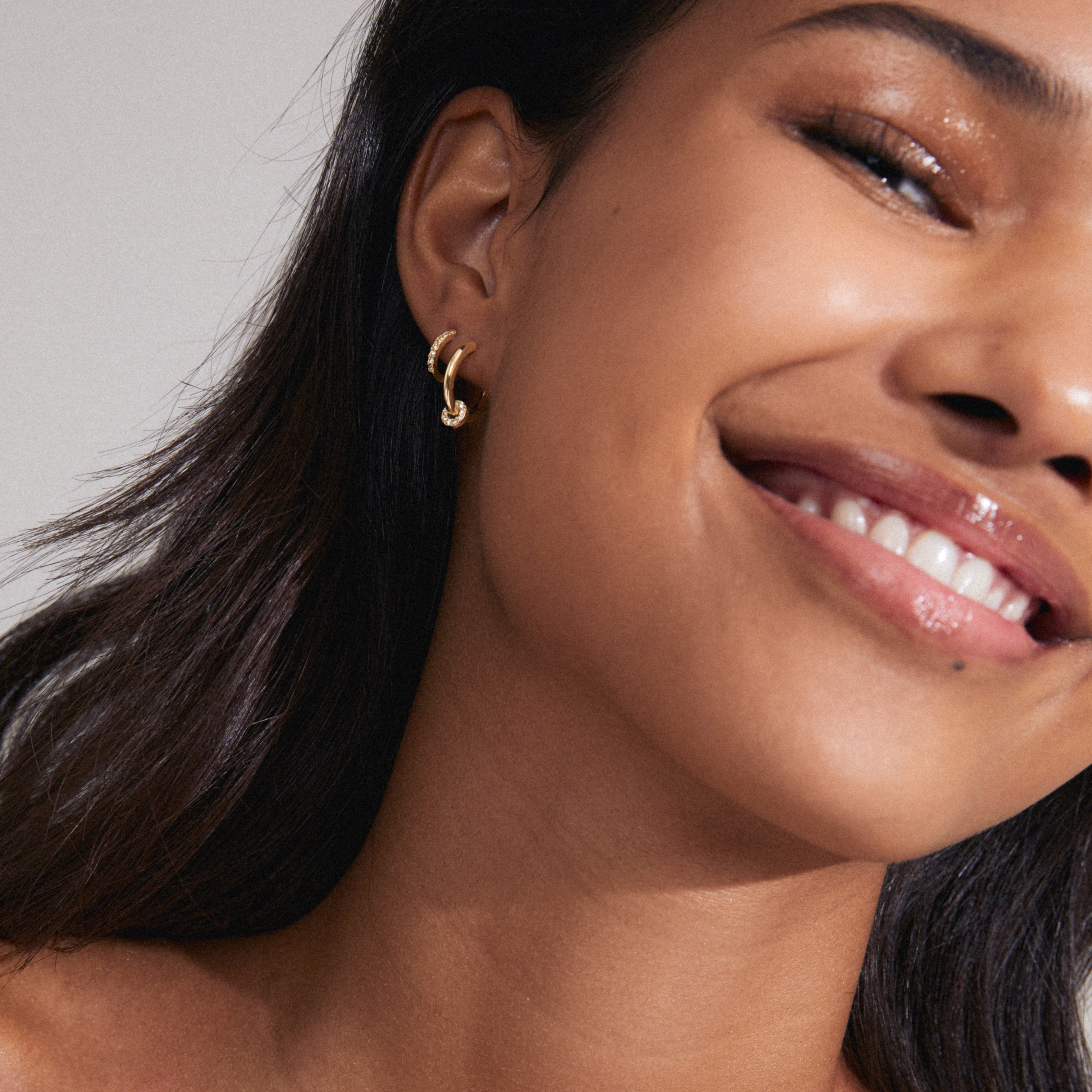 SCOTTIE earrings 2-in-1 set gold-plated, featuring huggie hoops with Preciosa crystals and shiny hoops with detachable crystal pendants, worn by a smiling woman.