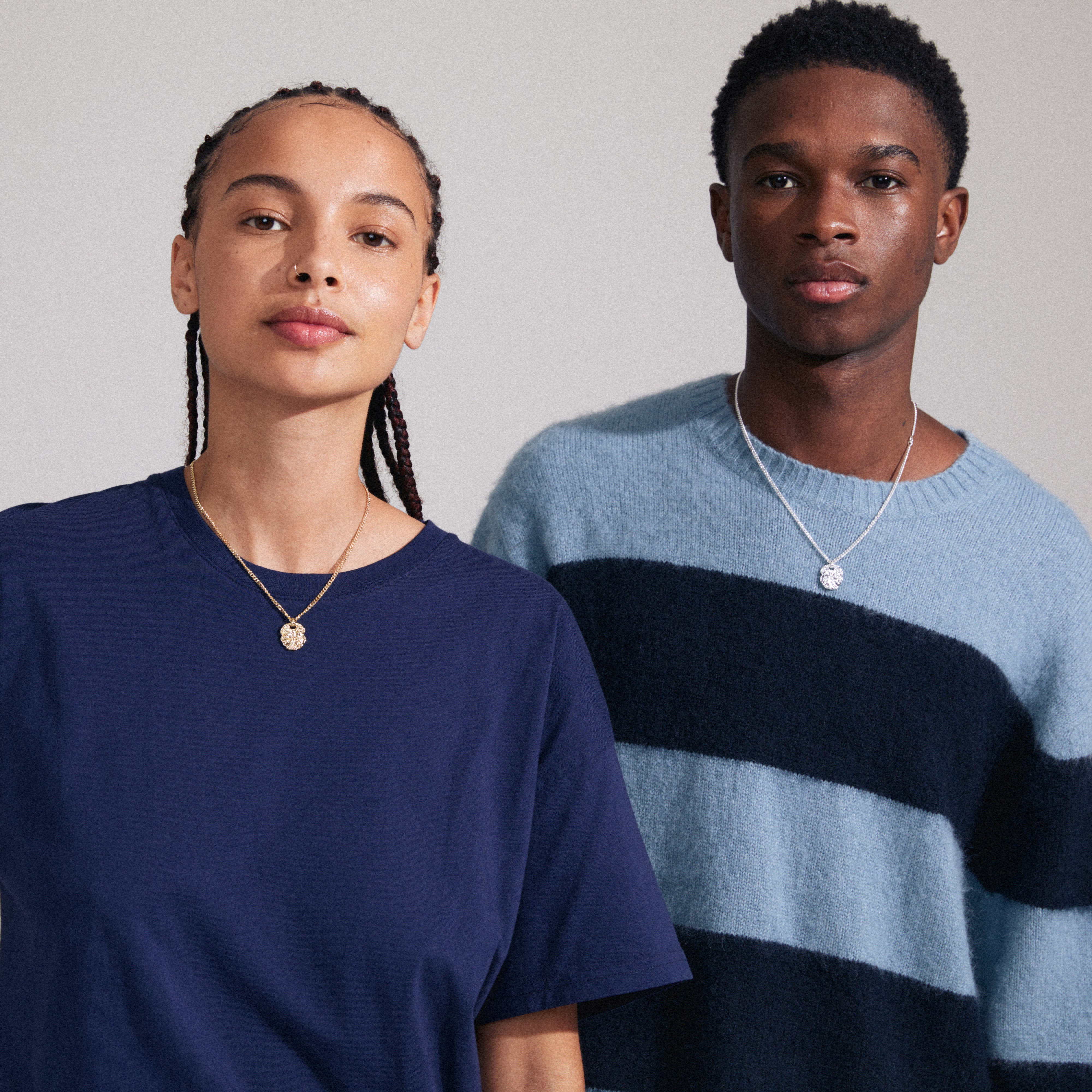 The SCOTTIE coin necklace, silver-plated with a rustic coin pendant on a sleek curb chain, worn by a stylish man and woman.