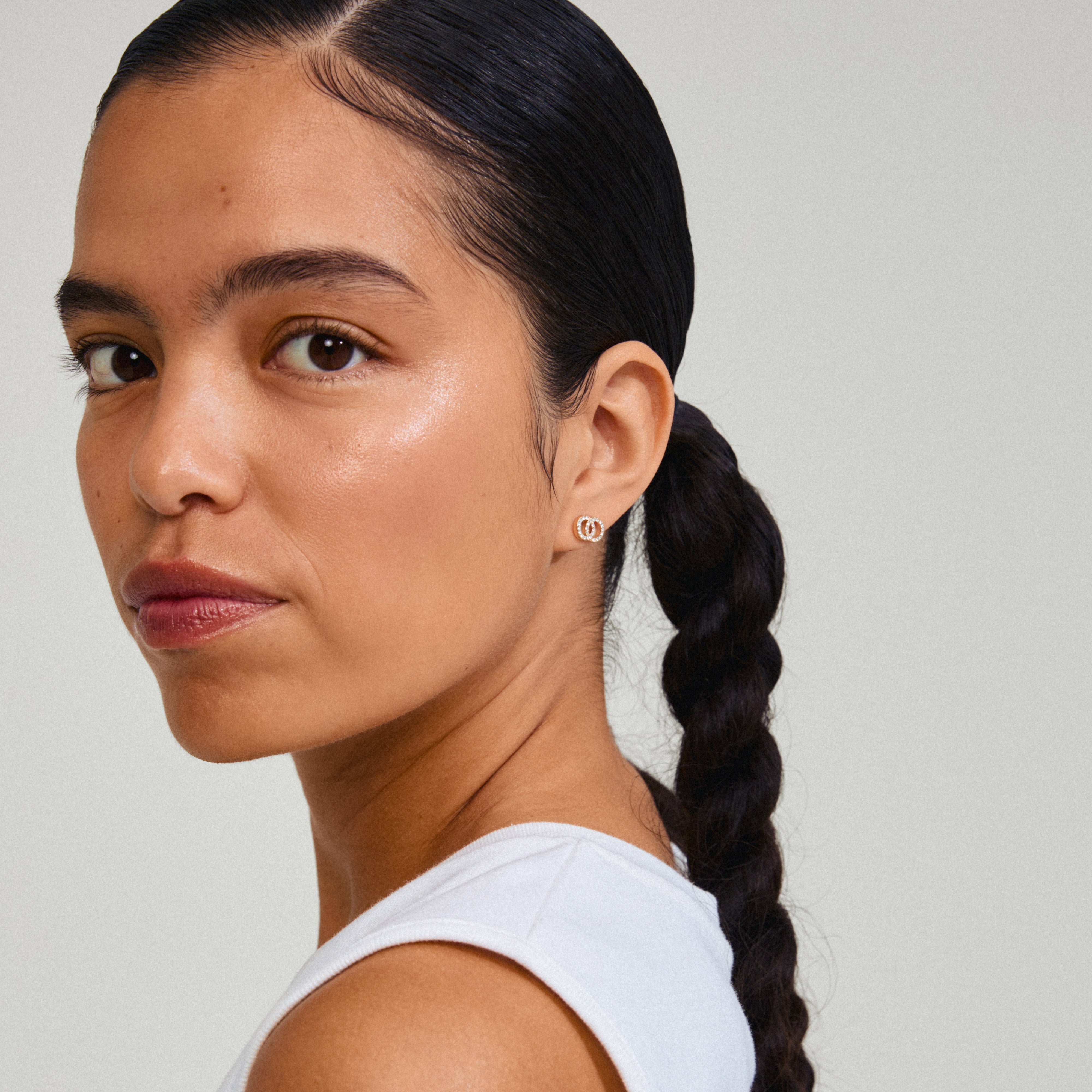 JOLINA recycled earrings gold-plated, featuring two intertwined halos with sparkling Preciosa crystals, worn by a woman with braided hair.