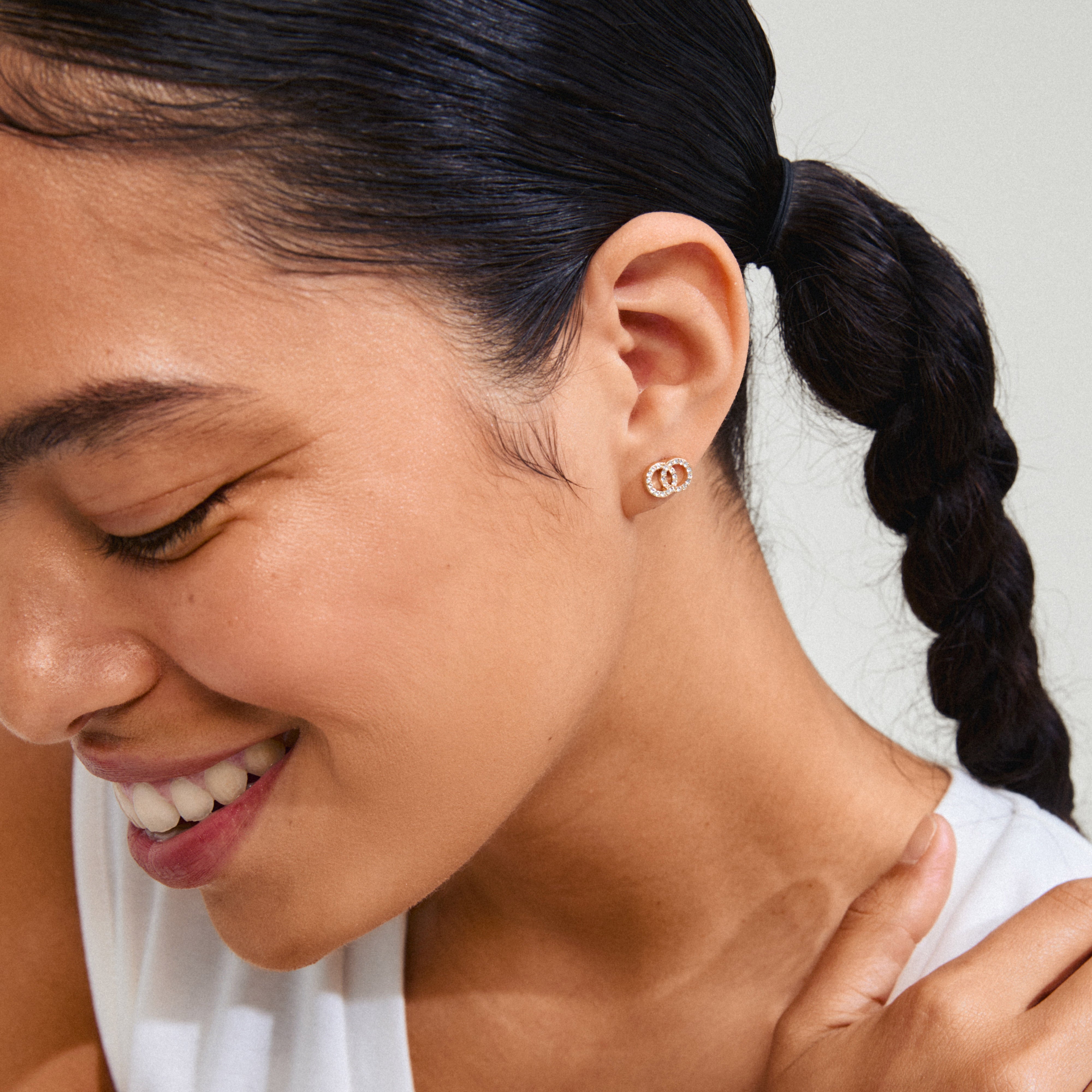 JOLINA recycled gold-plated earrings with sparkling Preciosa crystals, worn by a smiling woman, highlighting their intertwined halo design on her ear.