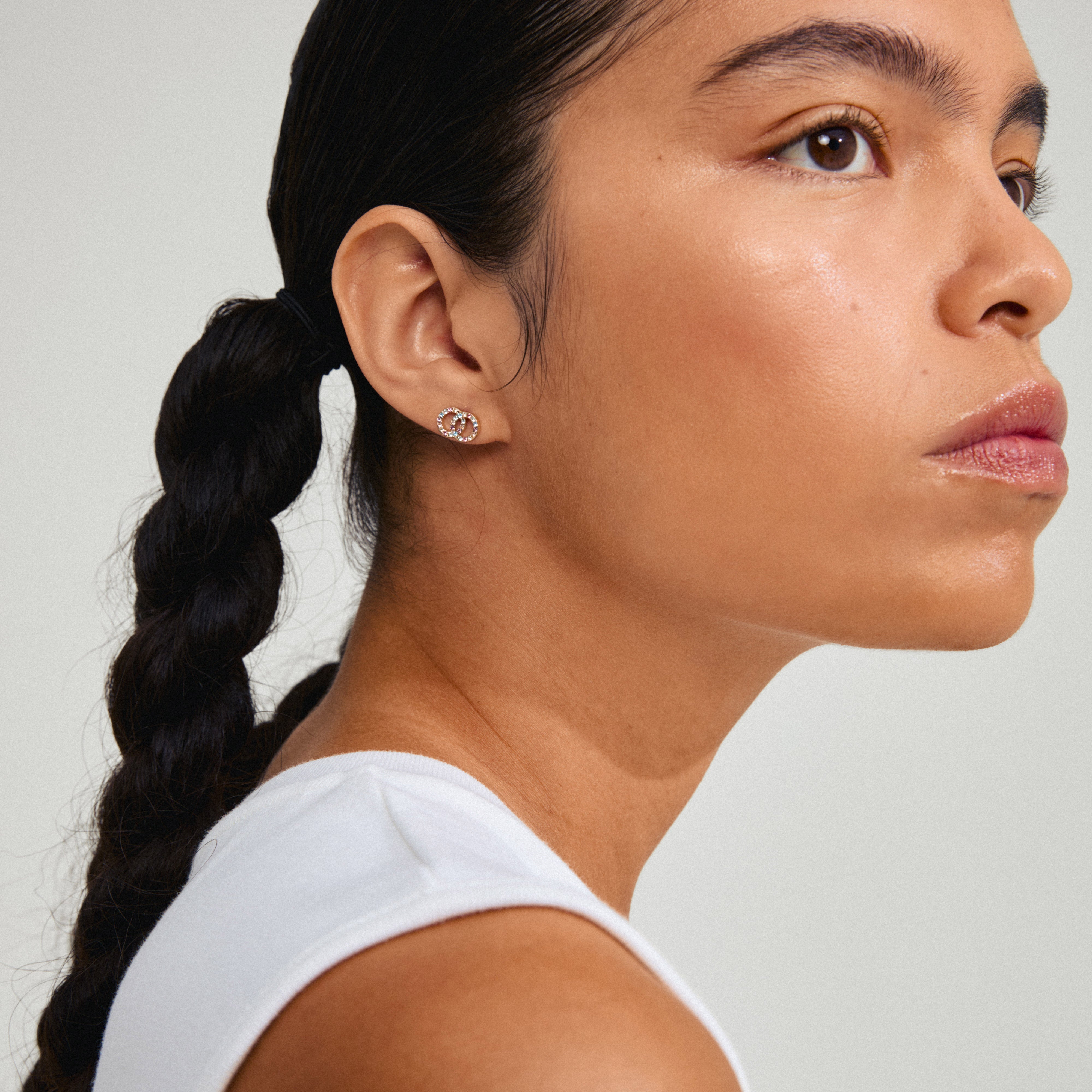 JOLINA recycled earrings, gold-plated with colorful stones, adorn a woman's ear, showcasing their intertwined halo design and eco-friendly craftsmanship.