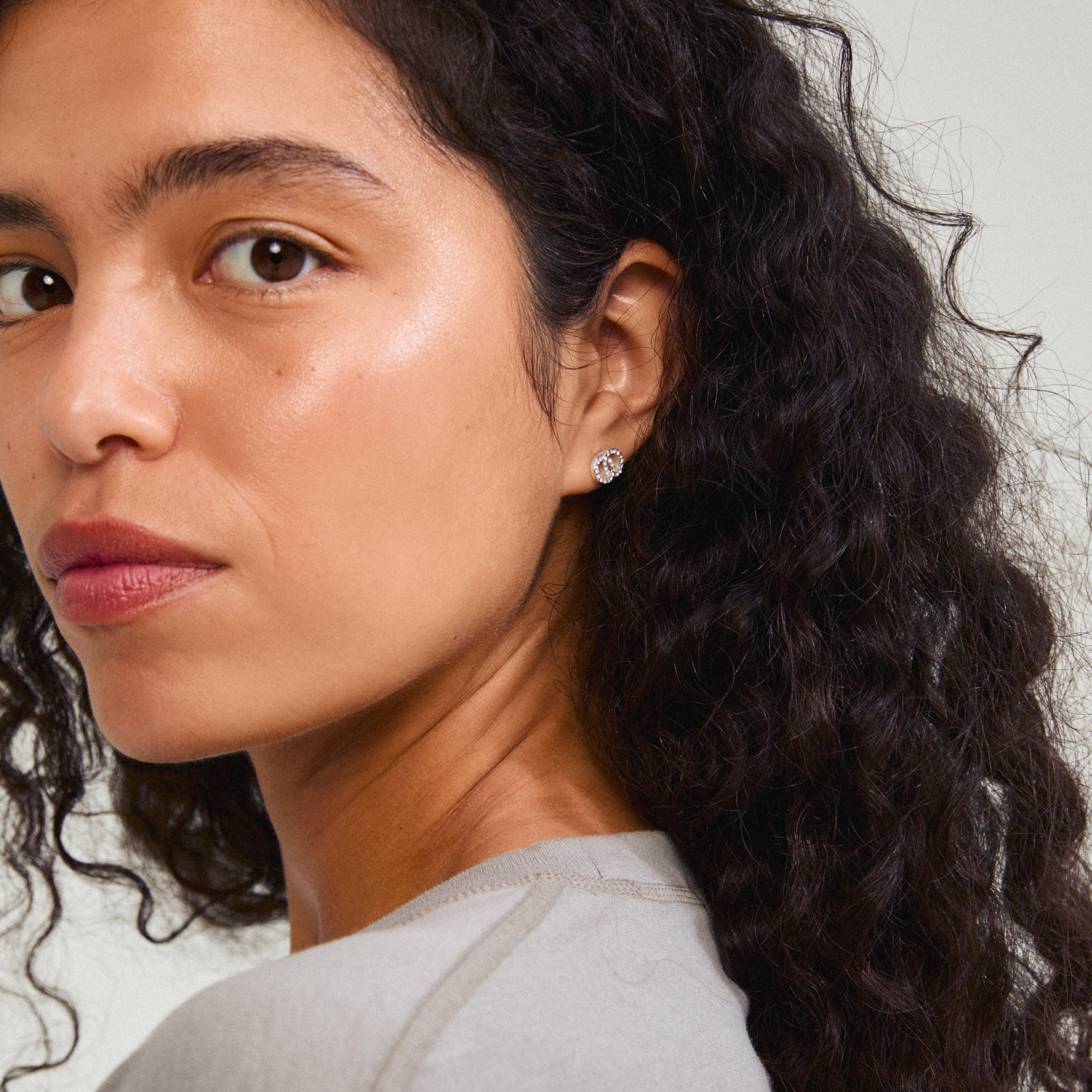 JOLINA recycled earrings silver-plated, featuring intertwined halos with sparkling Preciosa crystals, worn by a woman with long curly hair.