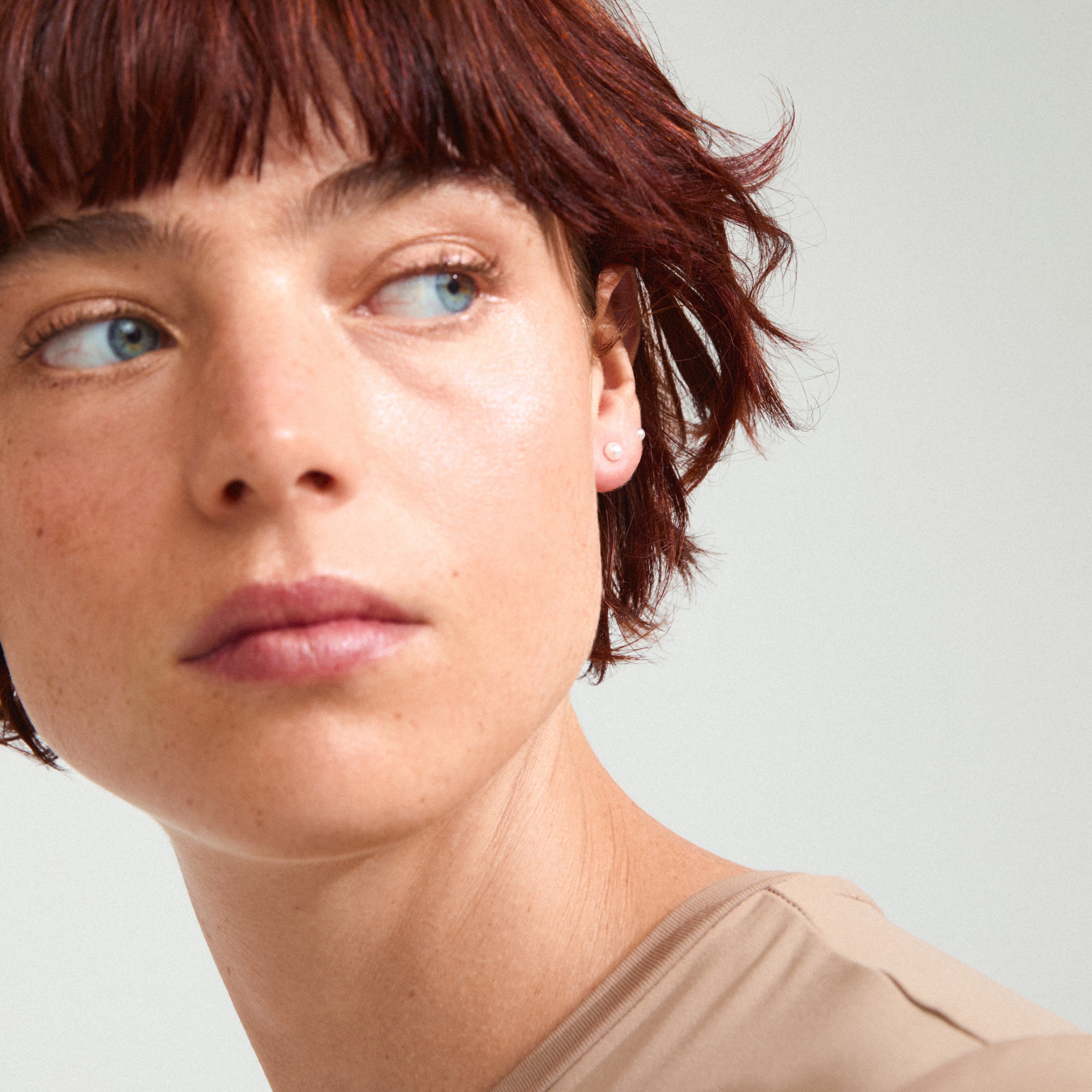 DAMARIS pearl earrings 2-in-1 set: Close-up of a woman showcasing elegant pearlescent glass bead stud earrings, highlighting their stylish simplicity and natural elegance.