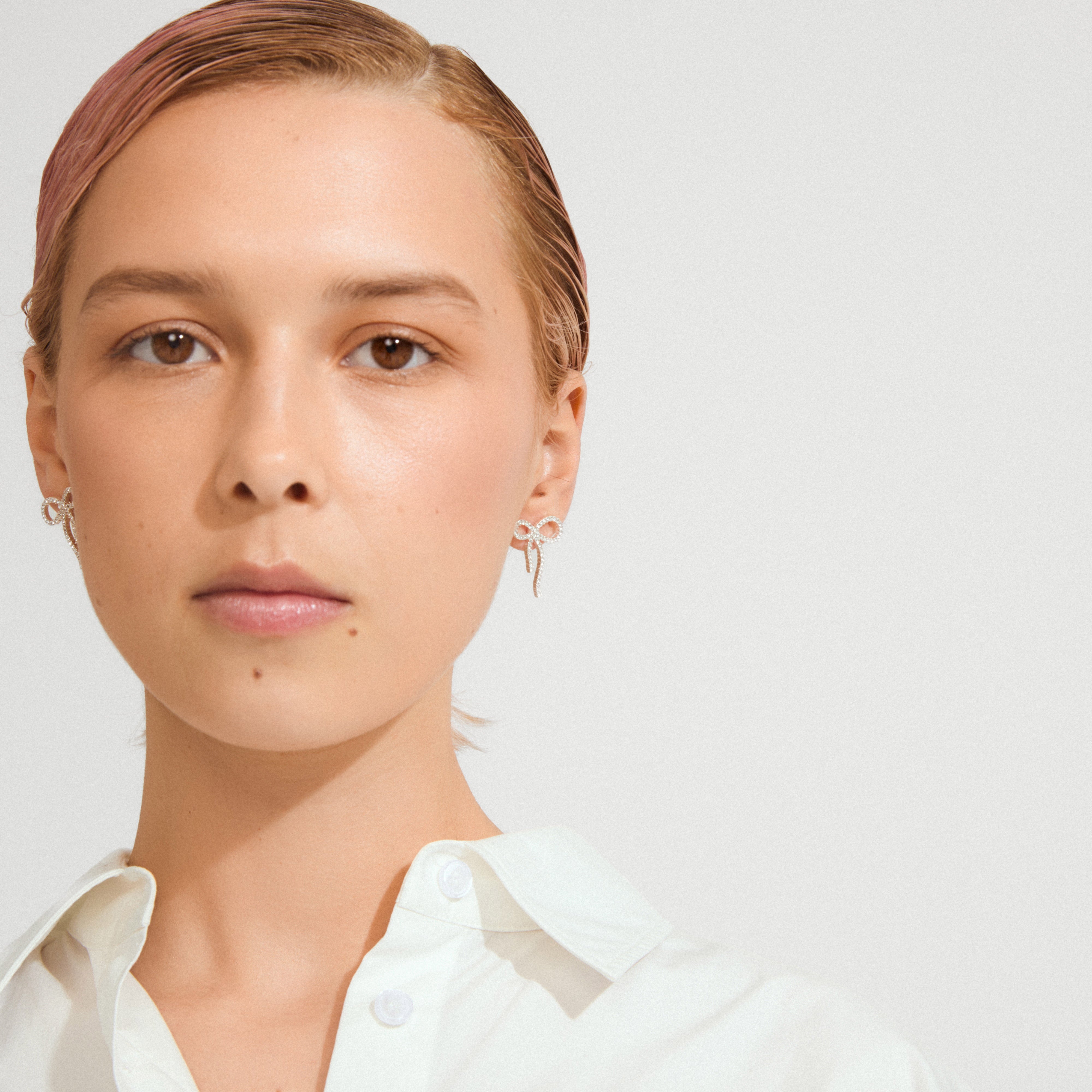 JOLANTA earrings silver-plated, featuring delicate looped bow design with sparkling Preciosa crystals, elegantly complement a white shirt for a chic, trendy look.