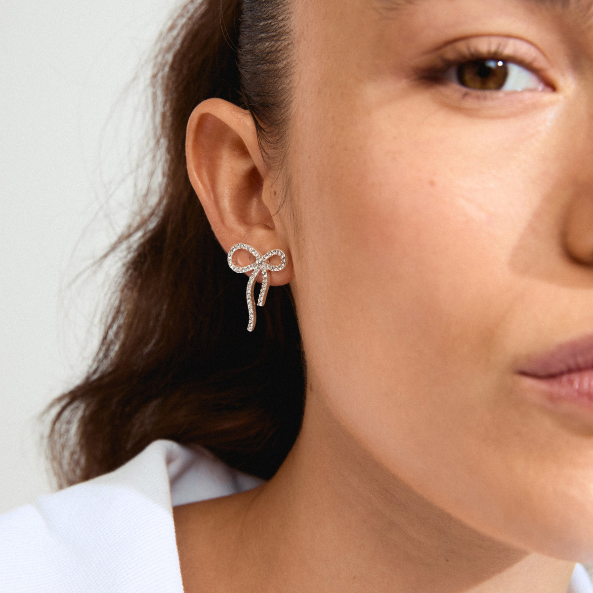 JOLANTA earrings silver-plated: Close-up of a woman's ear adorned with silver bow earrings featuring sparkling Preciosa crystals, showcasing trendy, eco-friendly Danish design.