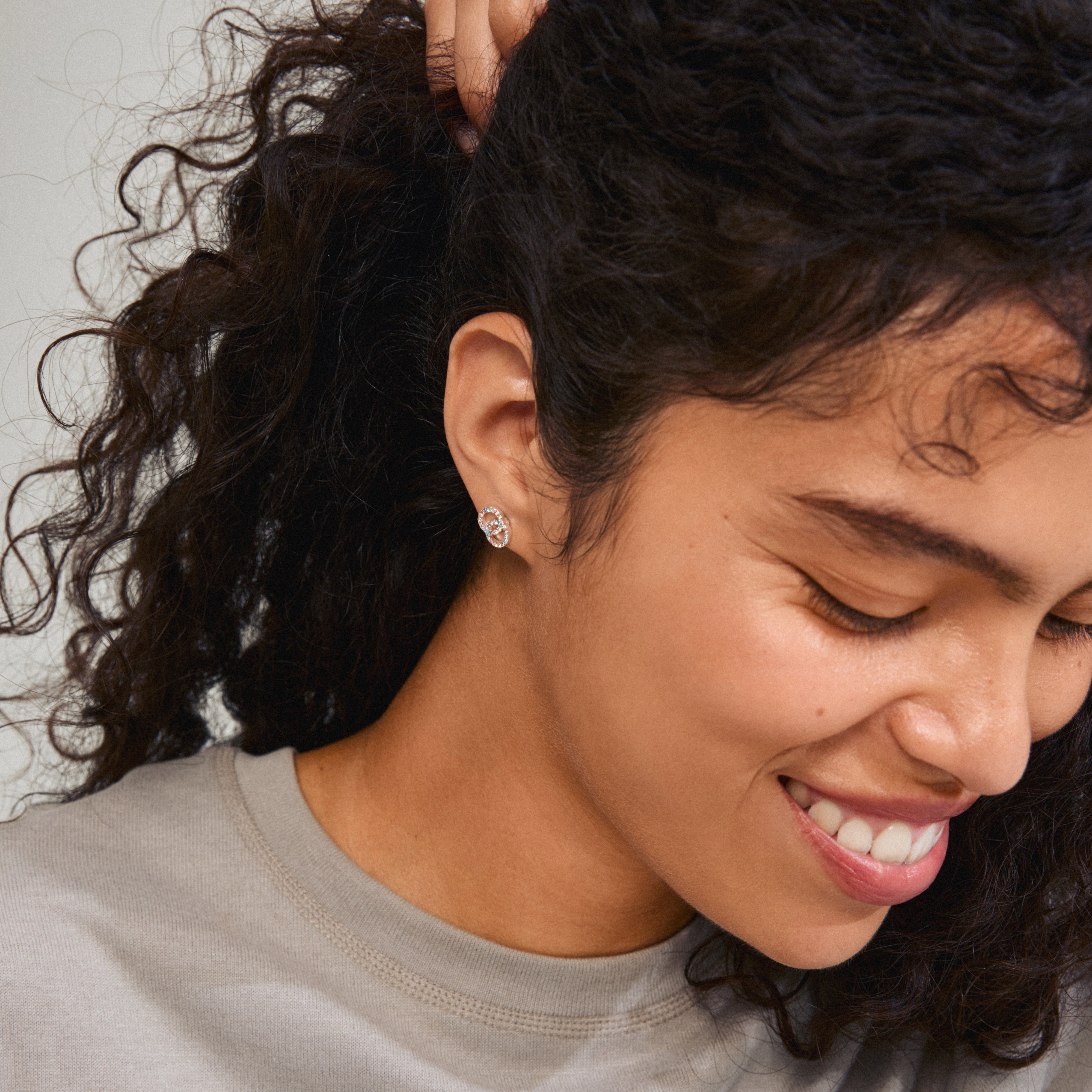 A woman wears JOLINA recycled earrings, featuring silver-plated intertwined halos with colorful crystals, highlighting their sparkle and eco-friendly craftsmanship.