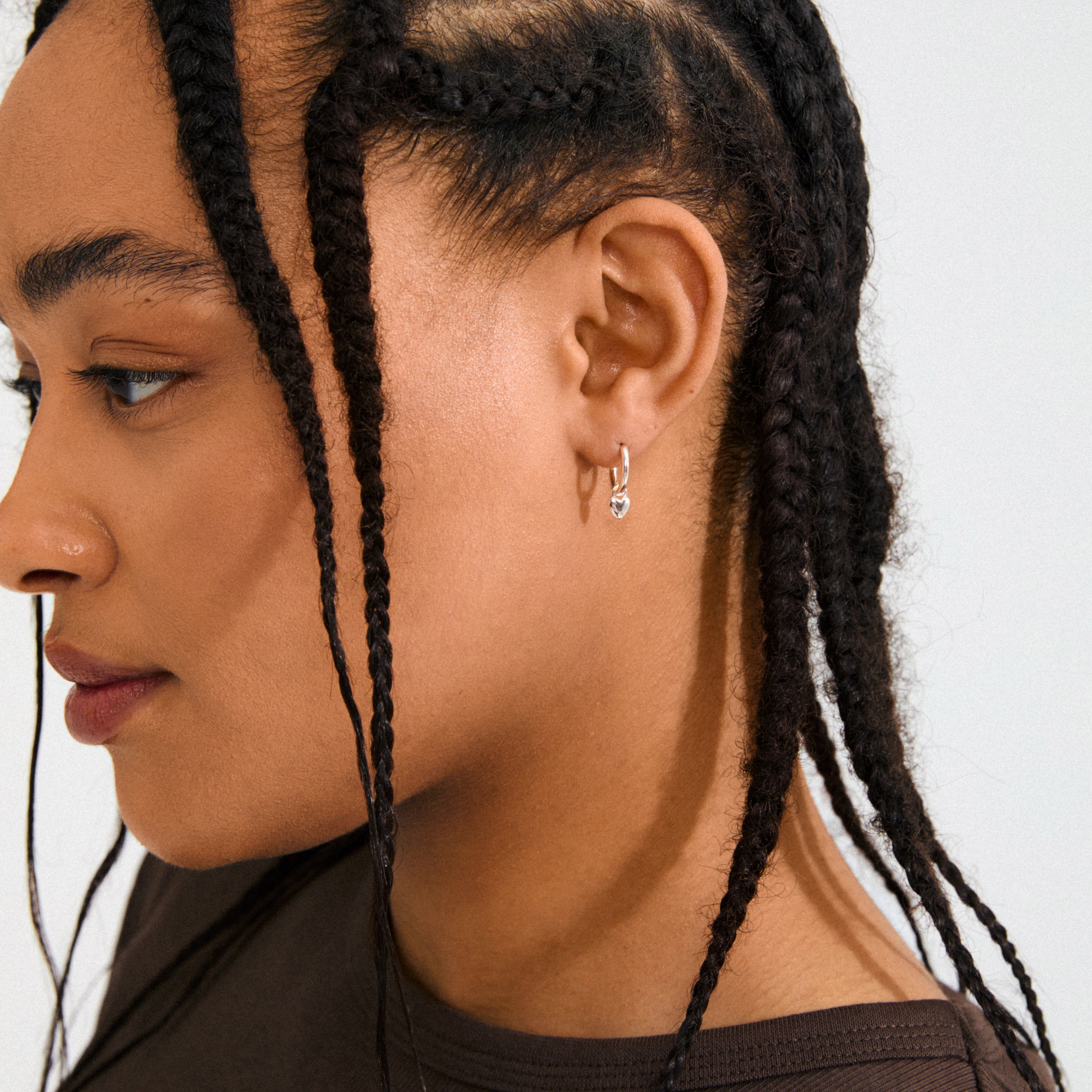 ALAIA earrings silver-plated feature petite heart pendants on huggie hoops, offering a romantic, versatile style crafted from 99% recycled material for everyday or special occasions.