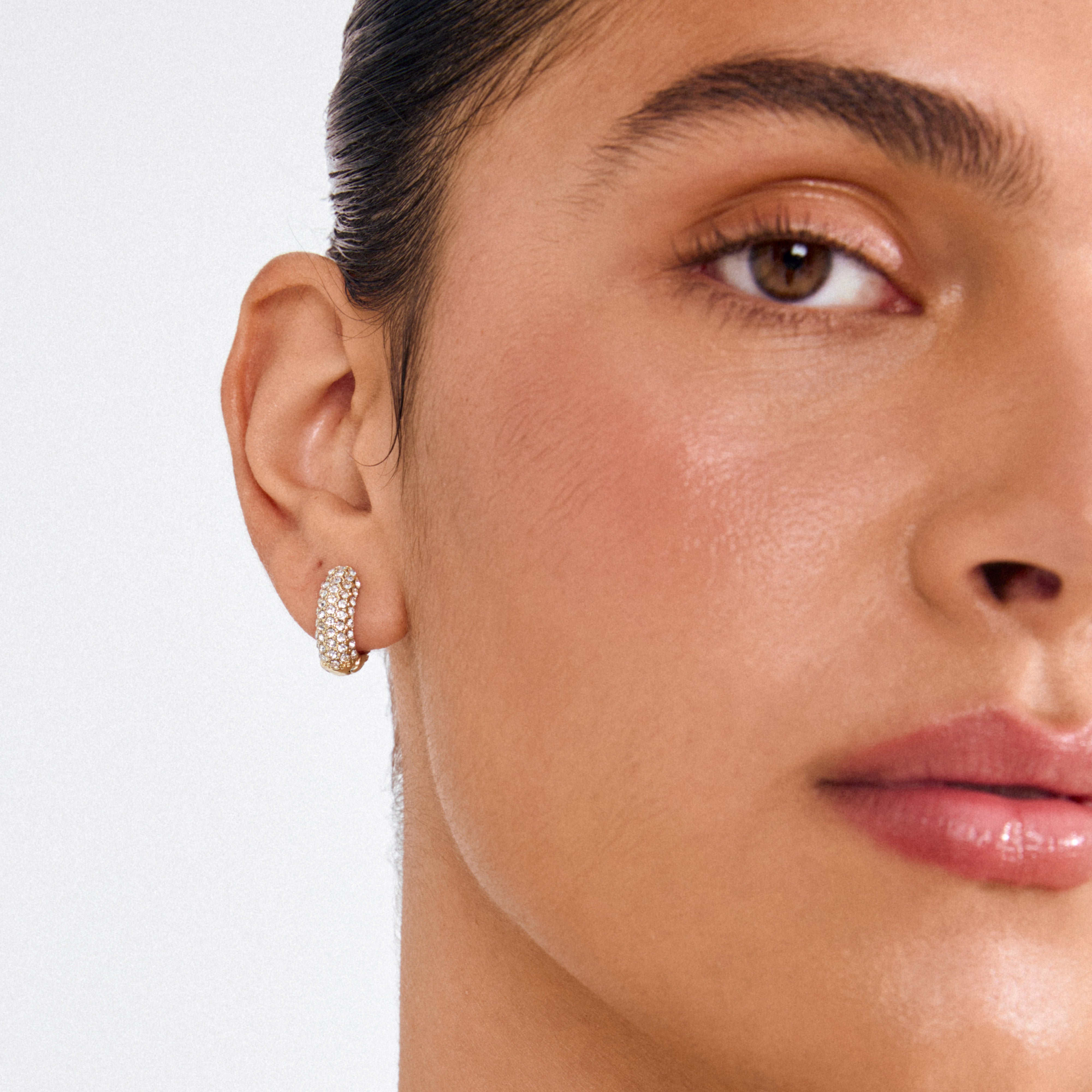 Close-up of a woman wearing LONA chunky crystal huggie hoops in gold, showcasing their sparkling Preciosa crystals and elegant design.