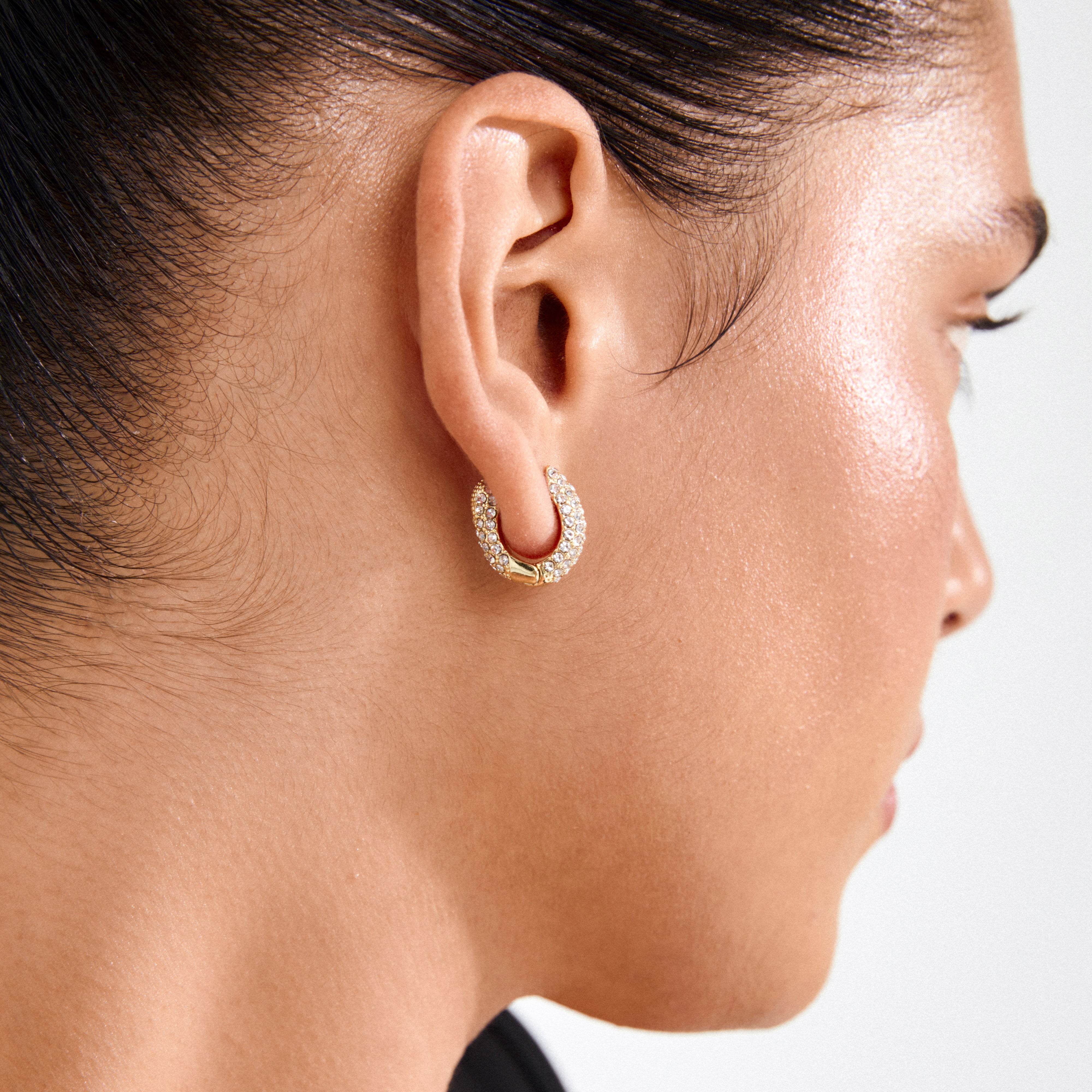 Profile view of an ear adorned with LONA chunky crystal huggie hoops, gold-plated and encrusted with Preciosa crystals, showcasing Pilgrim's commitment to style and sustainability.
