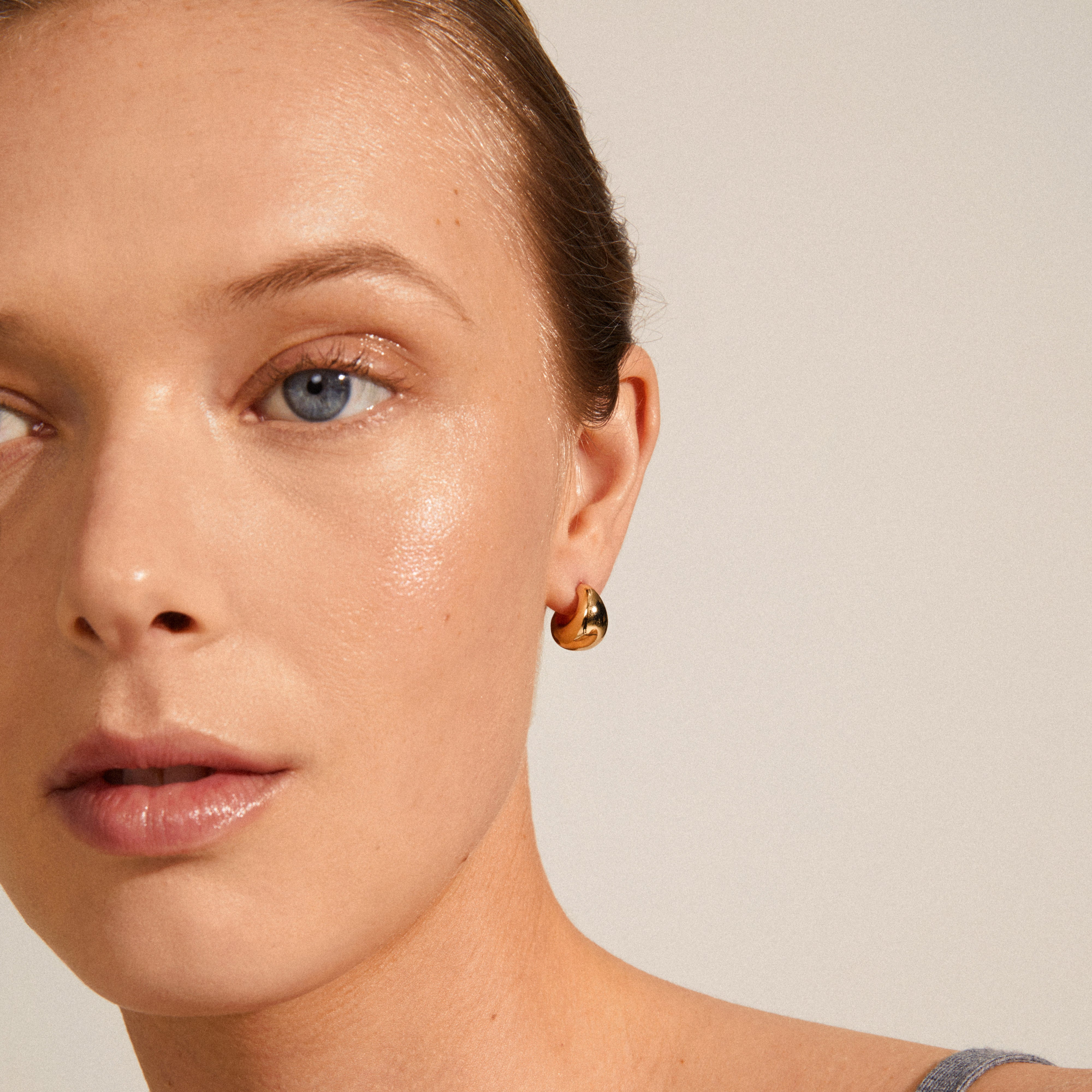 Close-up of a woman wearing ALEXANE chunky mini hoop earrings, gold-plated with a bold, classy design, highlighting Pilgrim's sustainable jewelry craftsmanship.