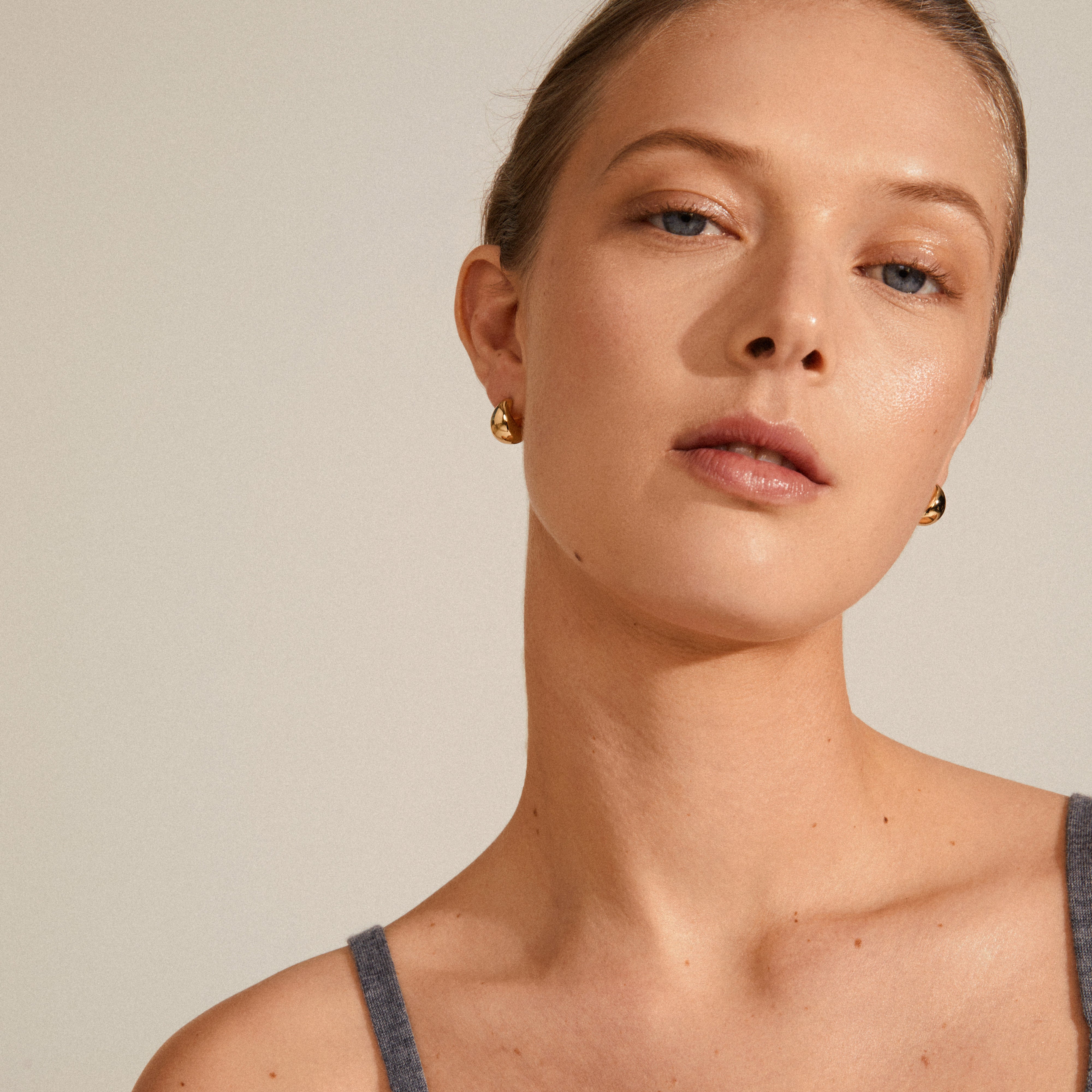 ALEXANE chunky mini hoop earrings gold-plated, showcased on a woman with a bun. The earrings add a bold, classy look, aligning with Pilgrim's eco-friendly collection.