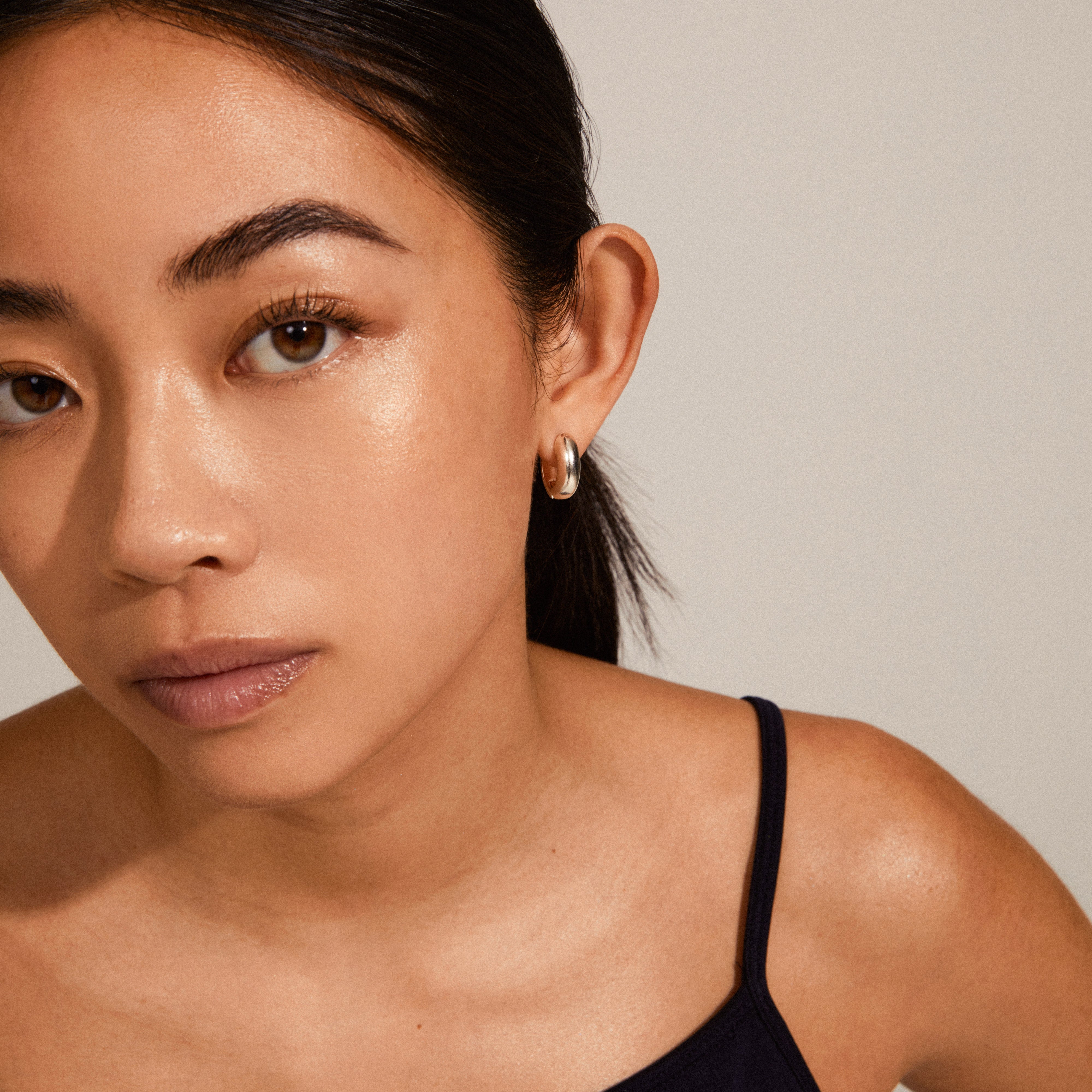 Woman wearing MINE chunky huggie hoops, silver-plated with a shiny, soft design, capturing a classy and feminine look. Perfect for effortless elegance.