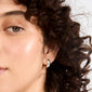Close-up of MINE chunky huggie hoops, silver-plated, on a person's ear with curly hair, showcasing their sculpted, high-shine design from Pilgrim's eco-conscious collection.