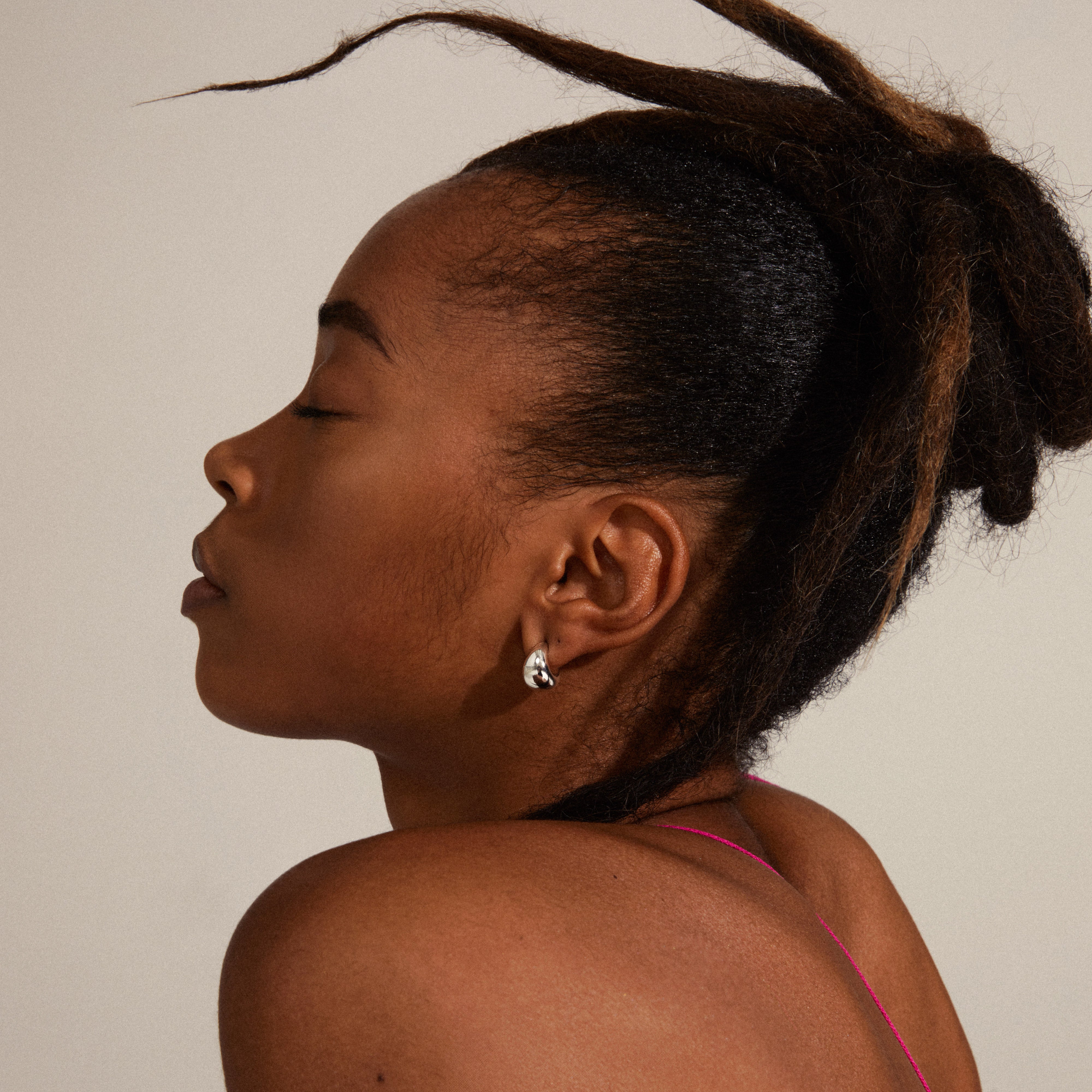 ALEXANE chunky mini hoop earrings, silver-plated, worn by a woman with hair pulled back, showcasing their trendy, shiny design from Pilgrim's recycled collection.