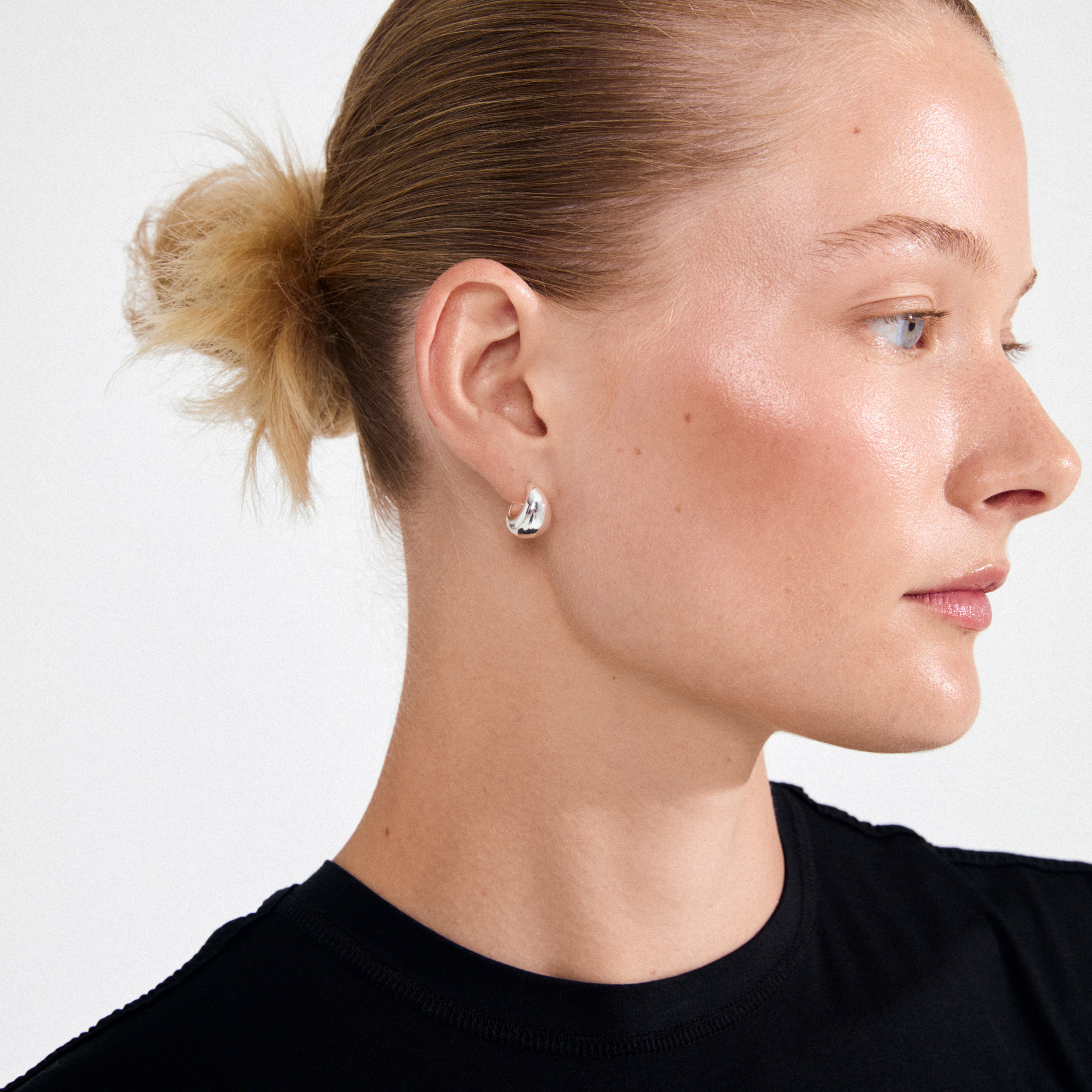 Profile of a person showcasing ALEXANE chunky mini hoop earrings, silver-plated, highlighting their teardrop shape and smooth finish for a retro, minimalist look.