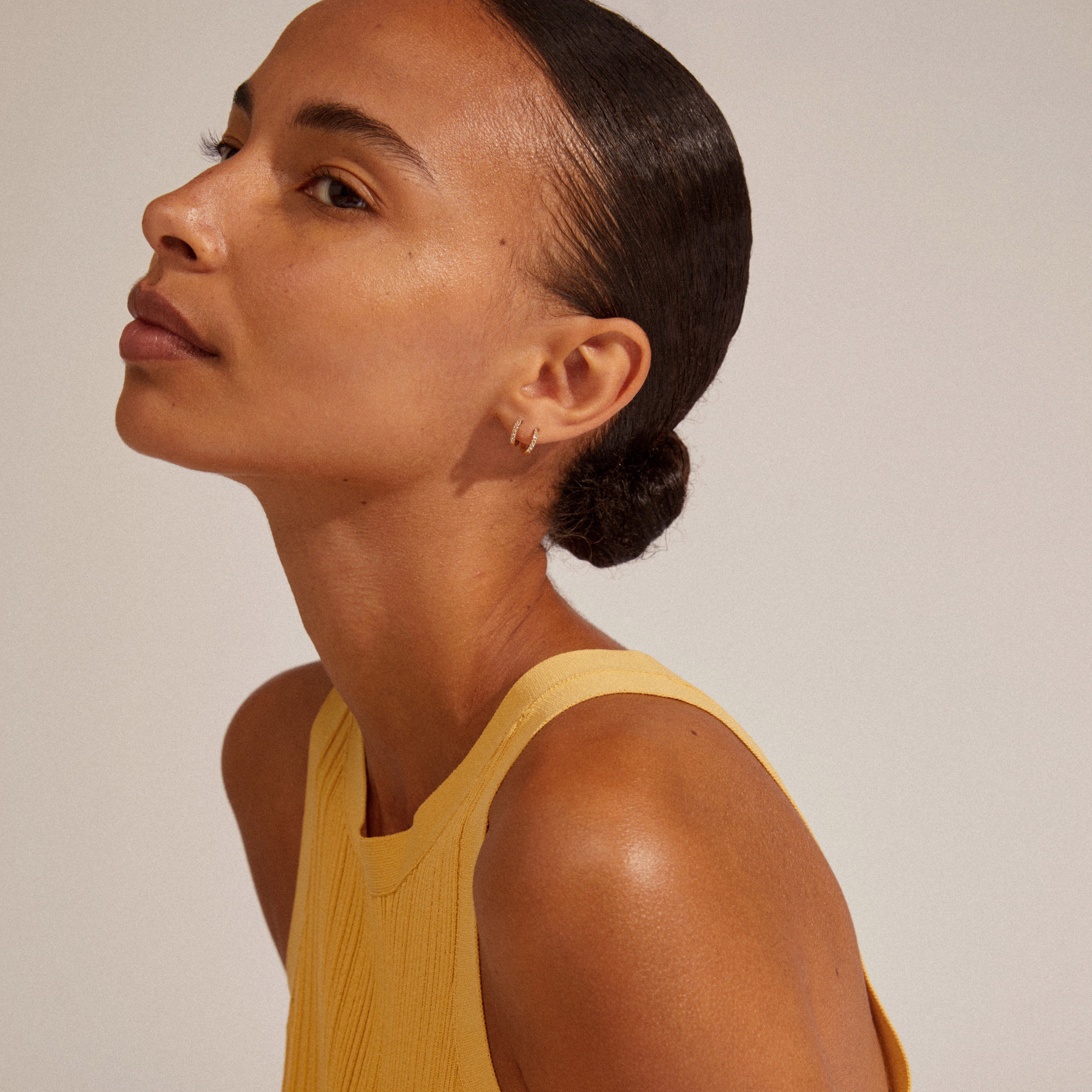 EBNA mini crystal huggie hoops gold-plated worn by woman with a bun, showcasing the gold-plated shine and clear Preciosa crystals.