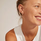 Woman wearing EBNA medium crystal hoops, gold-plated, smiling. Showcasing stylish Preciosa crystal earrings with a smart click lock for easy use.