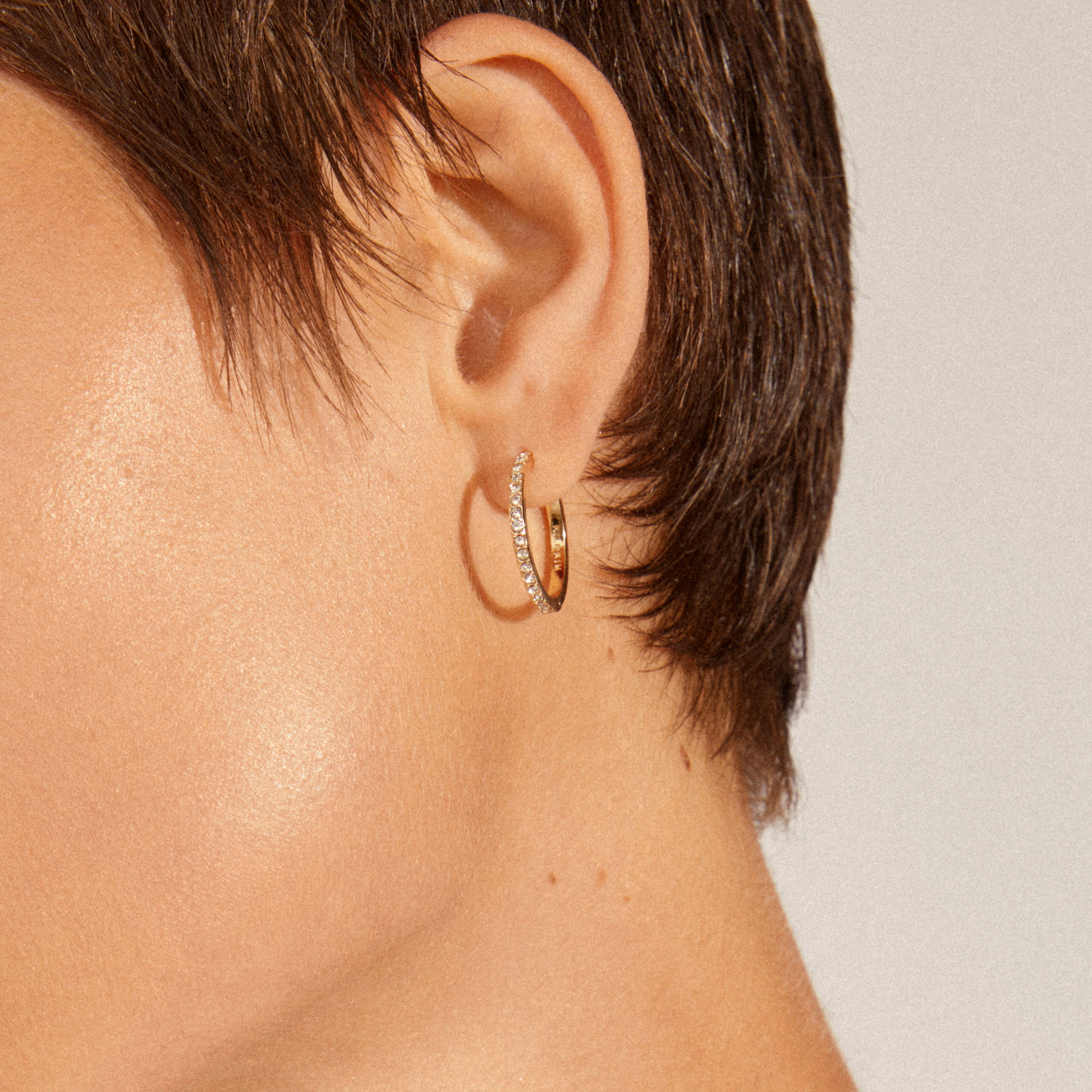 Close-up of EBNA large crystal hoops gold-plated on an ear, showcasing one polished hoop and one crystal-studded hoop, highlighting their sparkle and elegant design.