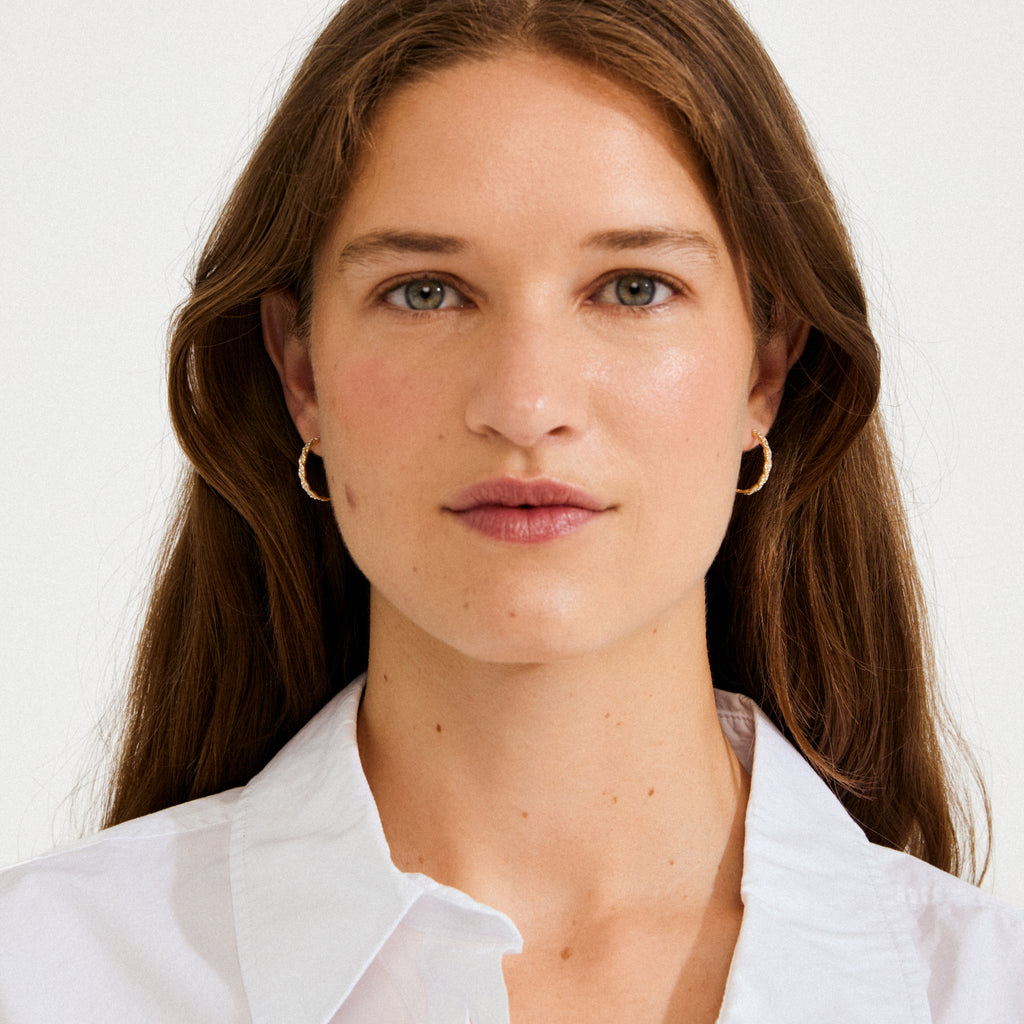 Woman wearing EZO twirled crystal hoops gold-plated, featuring shimmering twisted details and Preciosa crystals, showcasing a luxurious, dreamy vibe against a light background.
