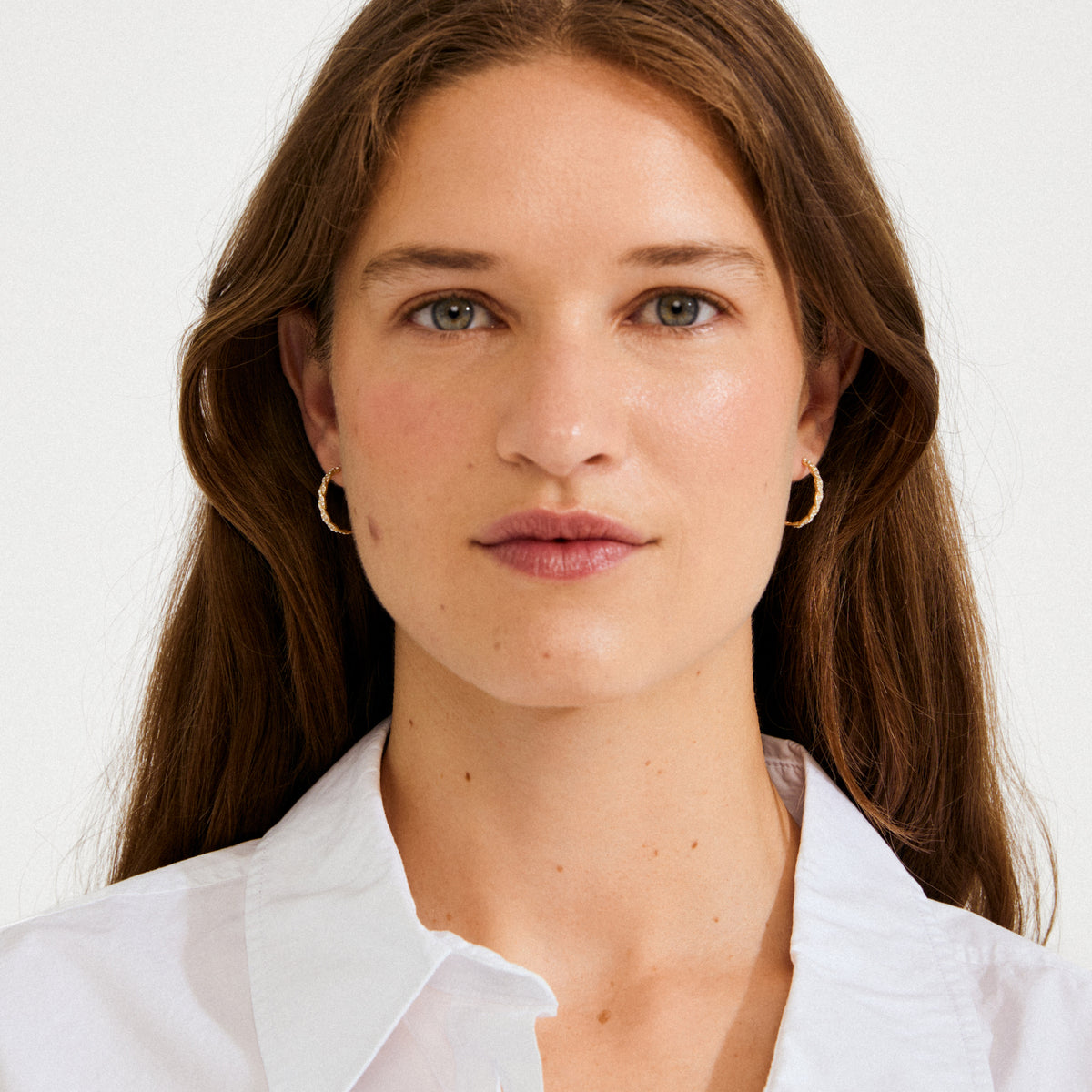 Woman wearing EZO twirled crystal hoops gold-plated, featuring shimmering twisted details and Preciosa crystals, showcasing a luxurious, dreamy vibe against a light background.