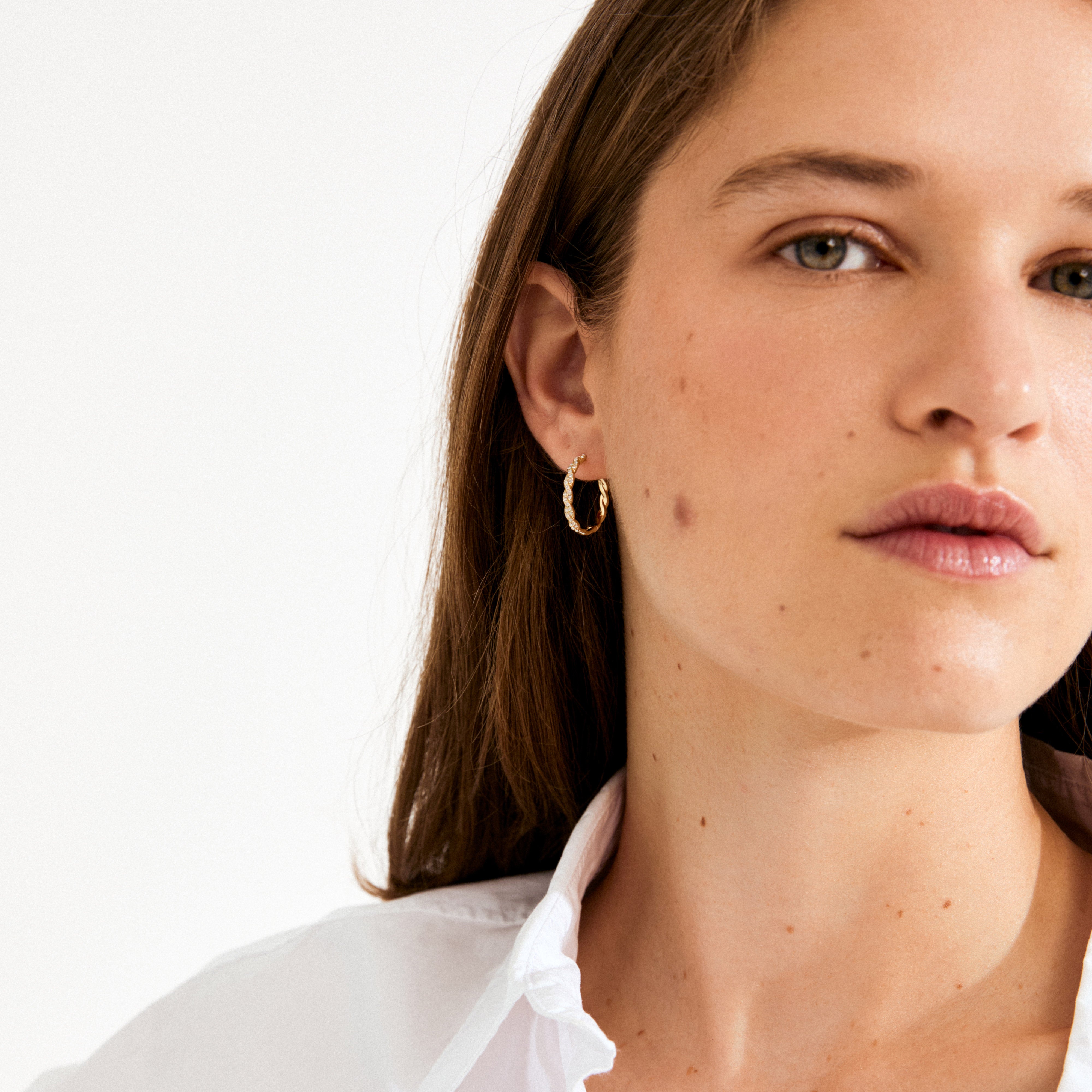 Close-up of a woman wearing EZO twirled crystal hoops gold-plated, showcasing their textured gold finish and shimmering crystals, complemented by her natural, understated look.