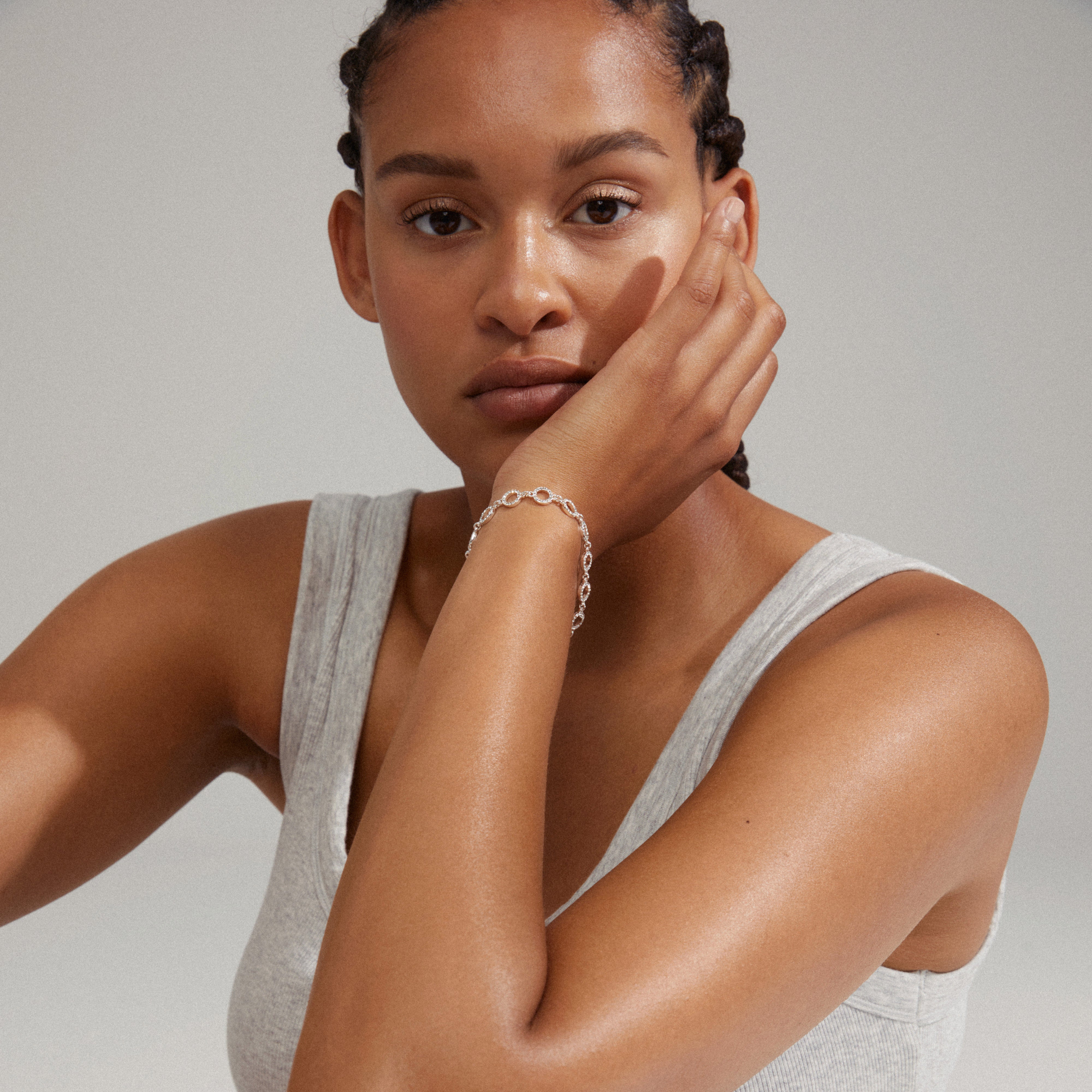 Woman with braids holds her face, showcasing the ROGUE crystal halo bracelet, silver-plated, adorned with sparkling Preciosa crystals from Pilgrim's collection.